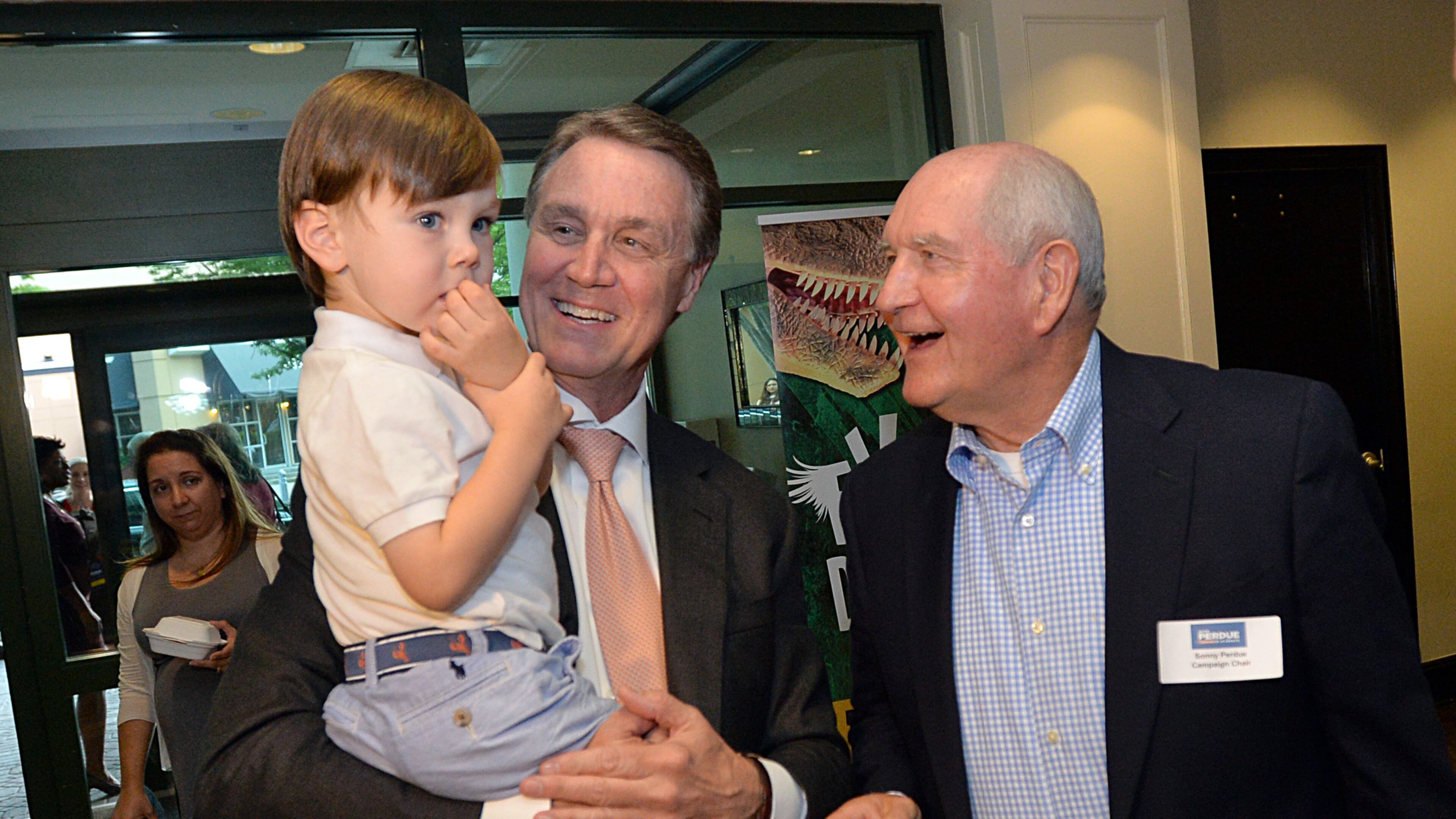 David Perdue holds his grandson David Perdue IV as former Gov. Sonny Perdue entertains the child. David Perdue, now a U.S. senator, helped sell Donald Trump on the idea of naming Sonny Perdue as his nominee for secretary of agriculture. HYOSUB SHIN / HSHIN@AJC.COM
