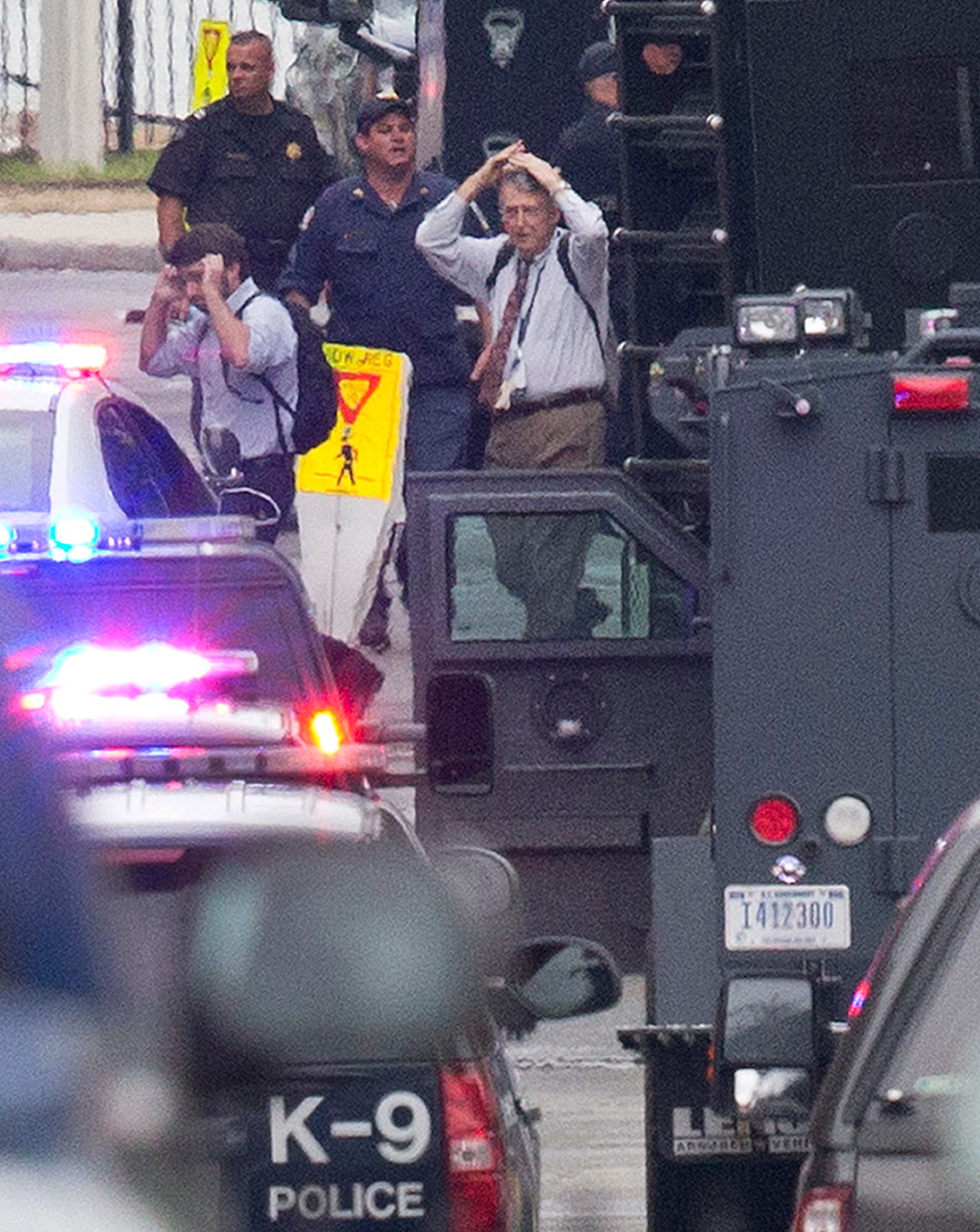 People hold their hands to their heads as they are escorted out of the building where a gunman was reported at the Washington Navy Yard in Washington, Monday, Sept. 16, 2013.