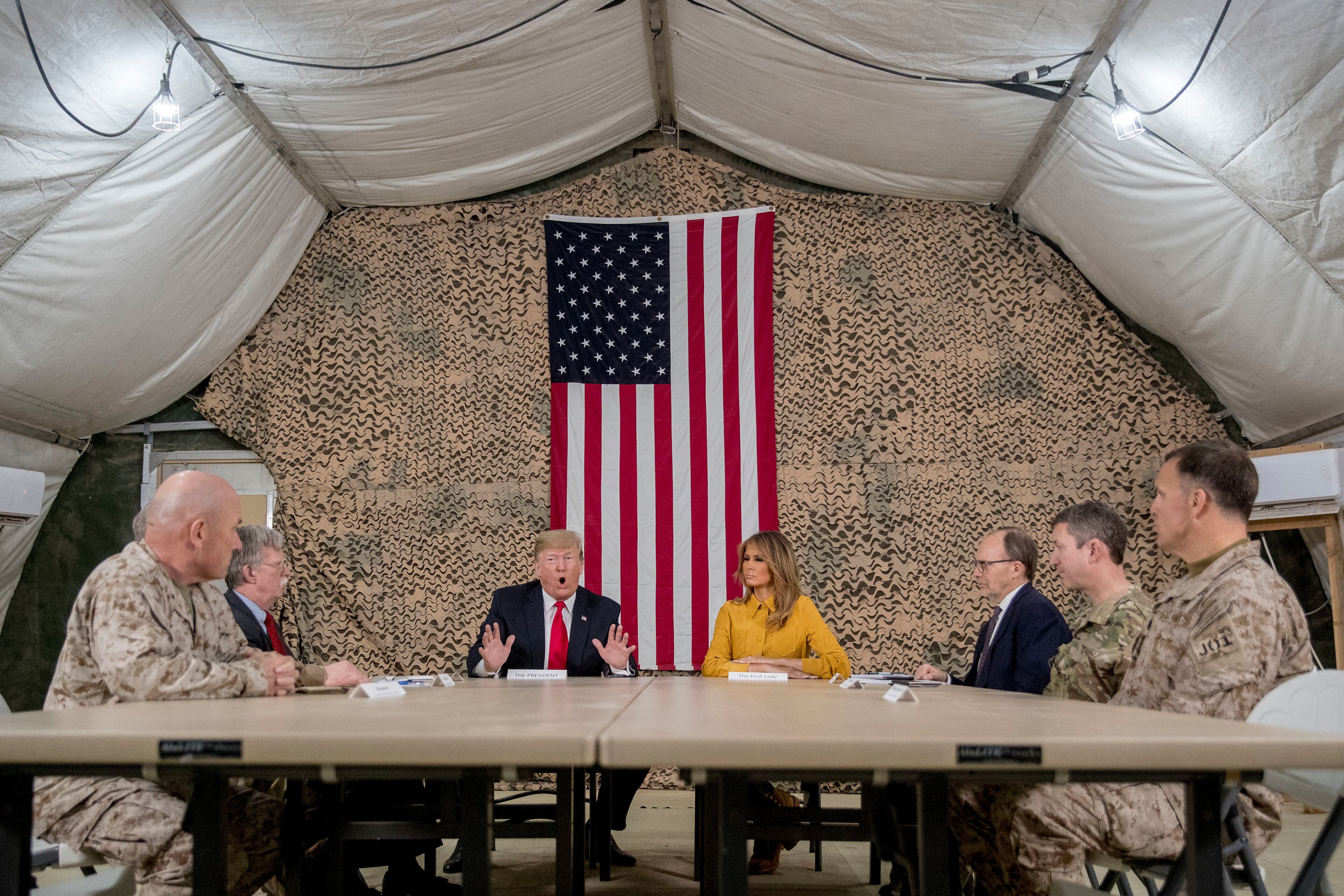 President Donald Trump, accompanied by National Security Adviser John Bolton, third from left, first lady Melania Trump, fourth from right, US Ambassador to Iraq Doug Silliman, third from right, and senior military leadership, speaks to members of the media at Al Asad Air Base, Iraq, Wednesday, Dec. 26, 2018. (AP Photo/Andrew Harnik)