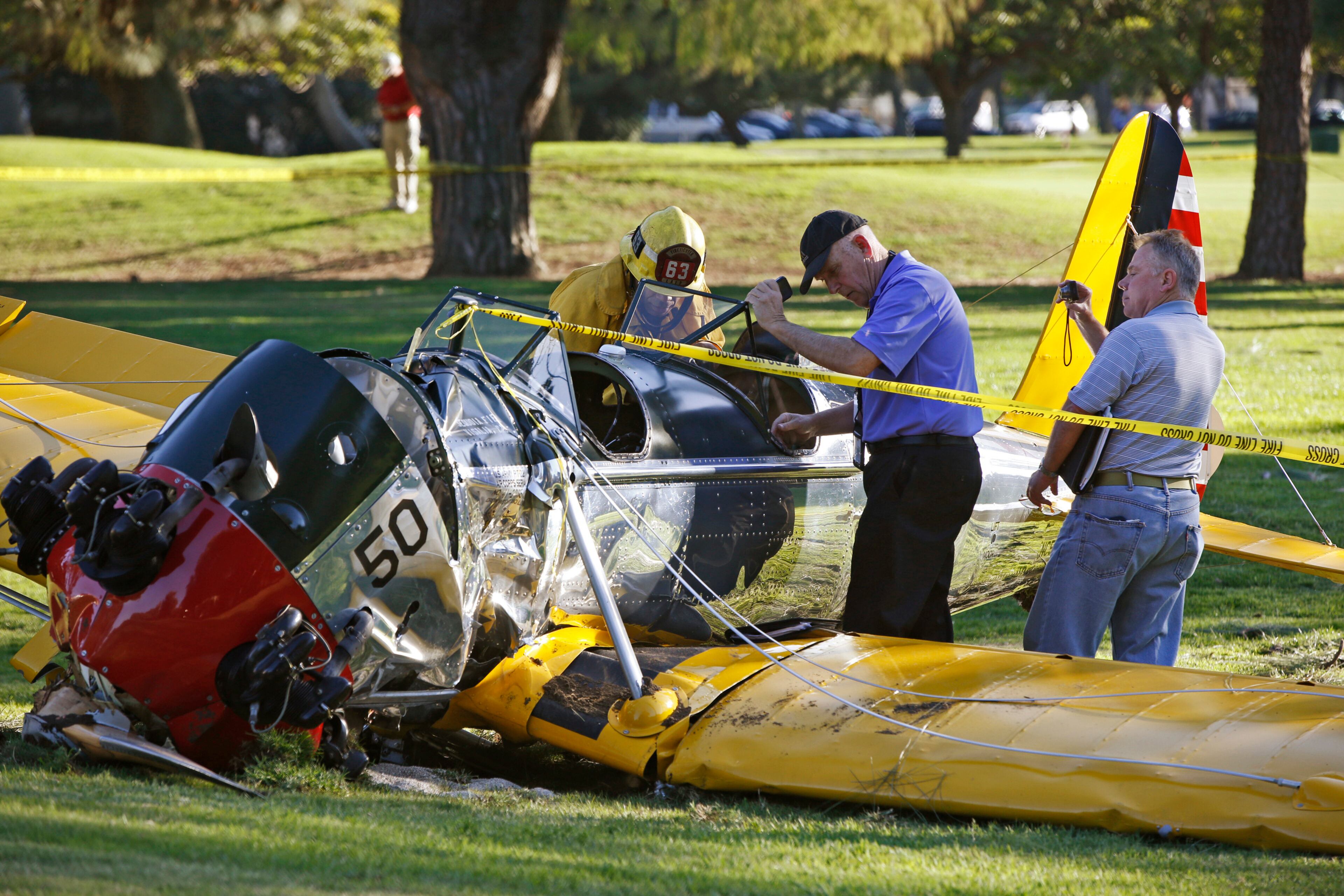 Officials work on the scene of a vintage airplane that crash-landed on the Penmar Golf Course in the Venice area of Los Angeles, Thursday, March 5, 2015. Harrison Ford crash-landed the airplane shortly after taking off from a nearby airport and reporting engine problems. (AP Photo/Damian Dovarganes)