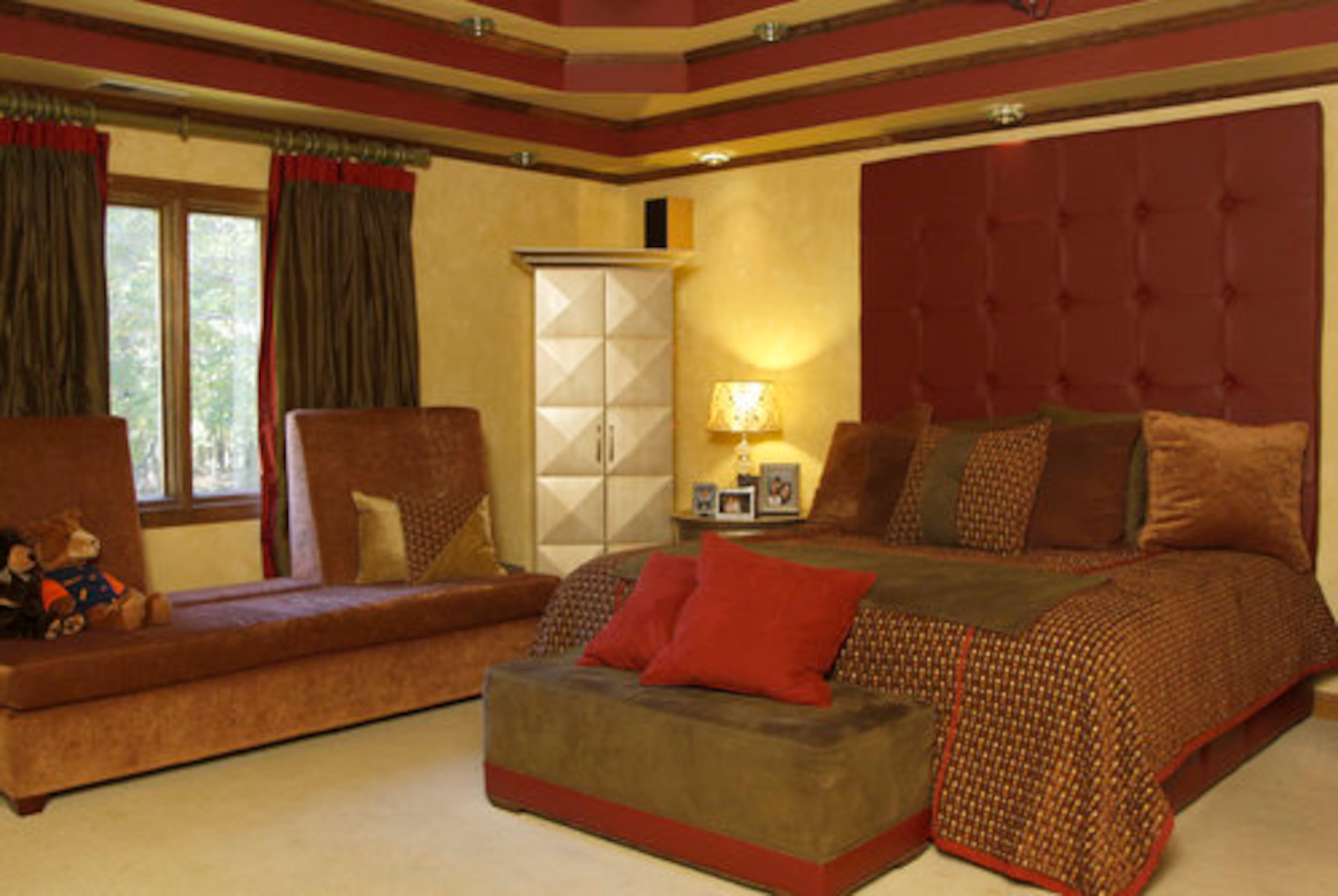 The master bedroom in the home of Kandi Burruss features a warm color scheme, with multiple ceiling trays and a custom bed. Burruss also had a retractable movie screen installed in this room, one of the splurges she indulged in when redecorating the home.