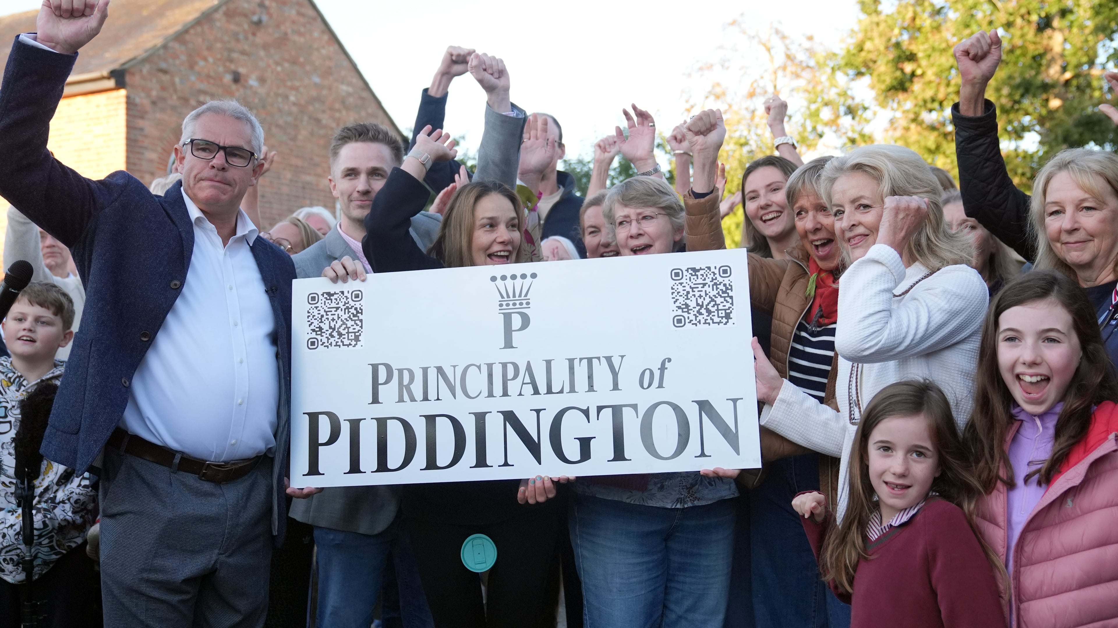 Local residents pose with a "Principality of Piddington" sign in the village of Piddington, Oxfordshire, England, Wednesday, Sept. 16, 2026, after they voted overwhelmingly to become an independent state in a symbolic "referendum". (Joe Giddens/PA via AP)