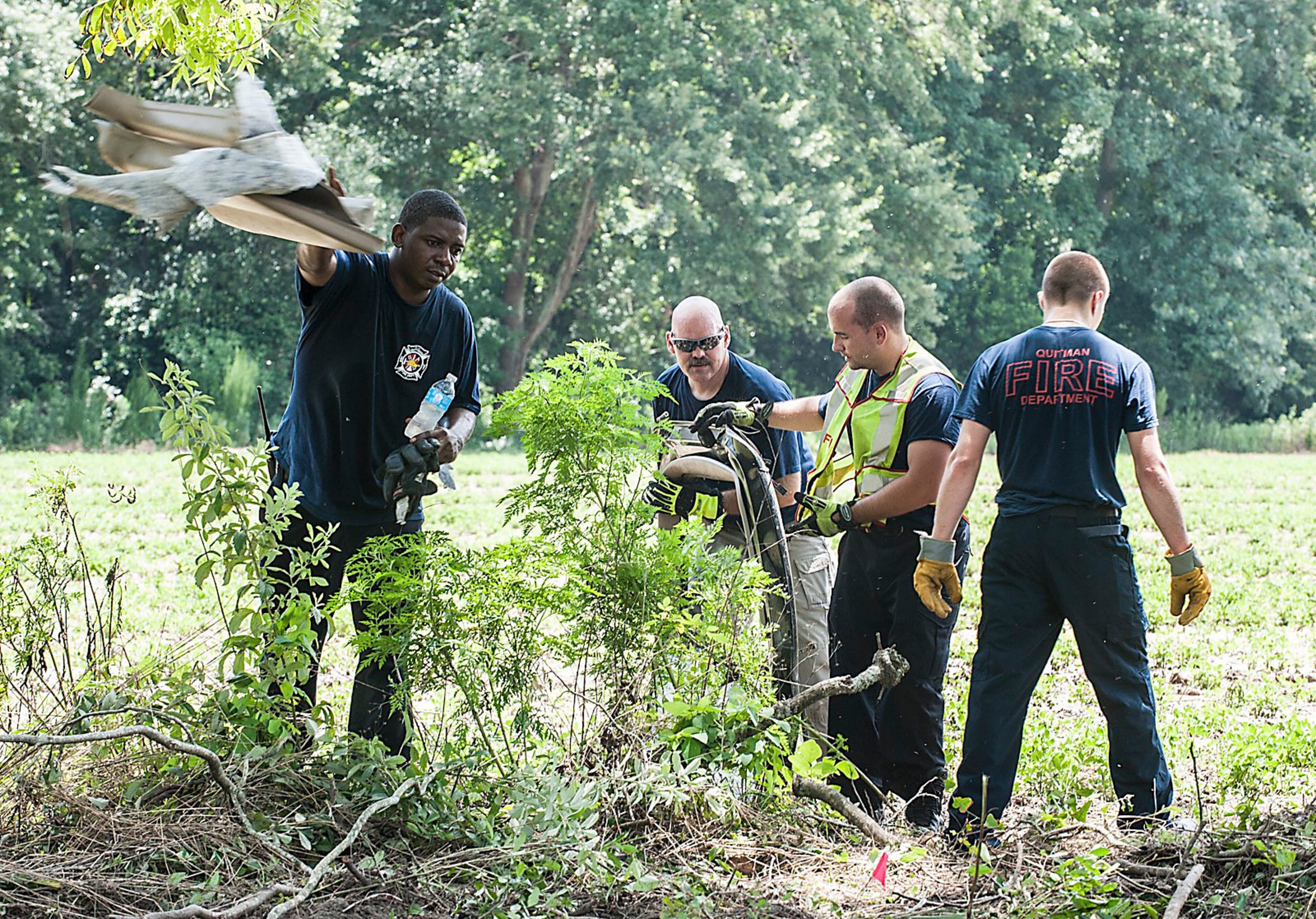 Members of the Quitman Fire Department recover debris scattered beside the roadway in a neighboring field.