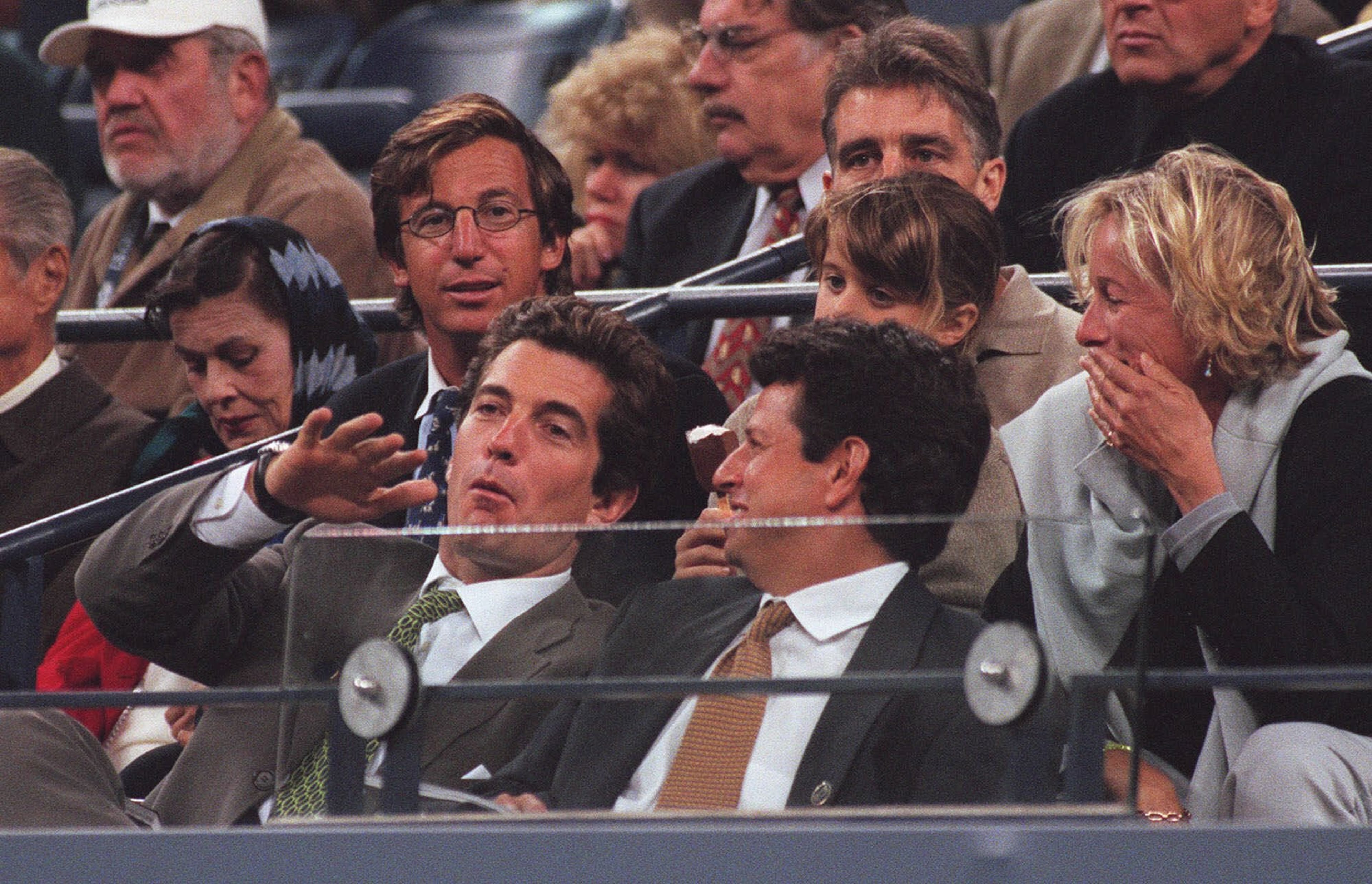 John F. Kennedy Jr., left, gestures to an unidentified friend while watching the quarterfinal match between Mark Philippoussis, of Australia, and Thomas Johansson, of Sweden, Thursday, Sept. 10, 1998 at the U.S. Open tennis tournament in New York. (AP Photo/Bill Kostroun)