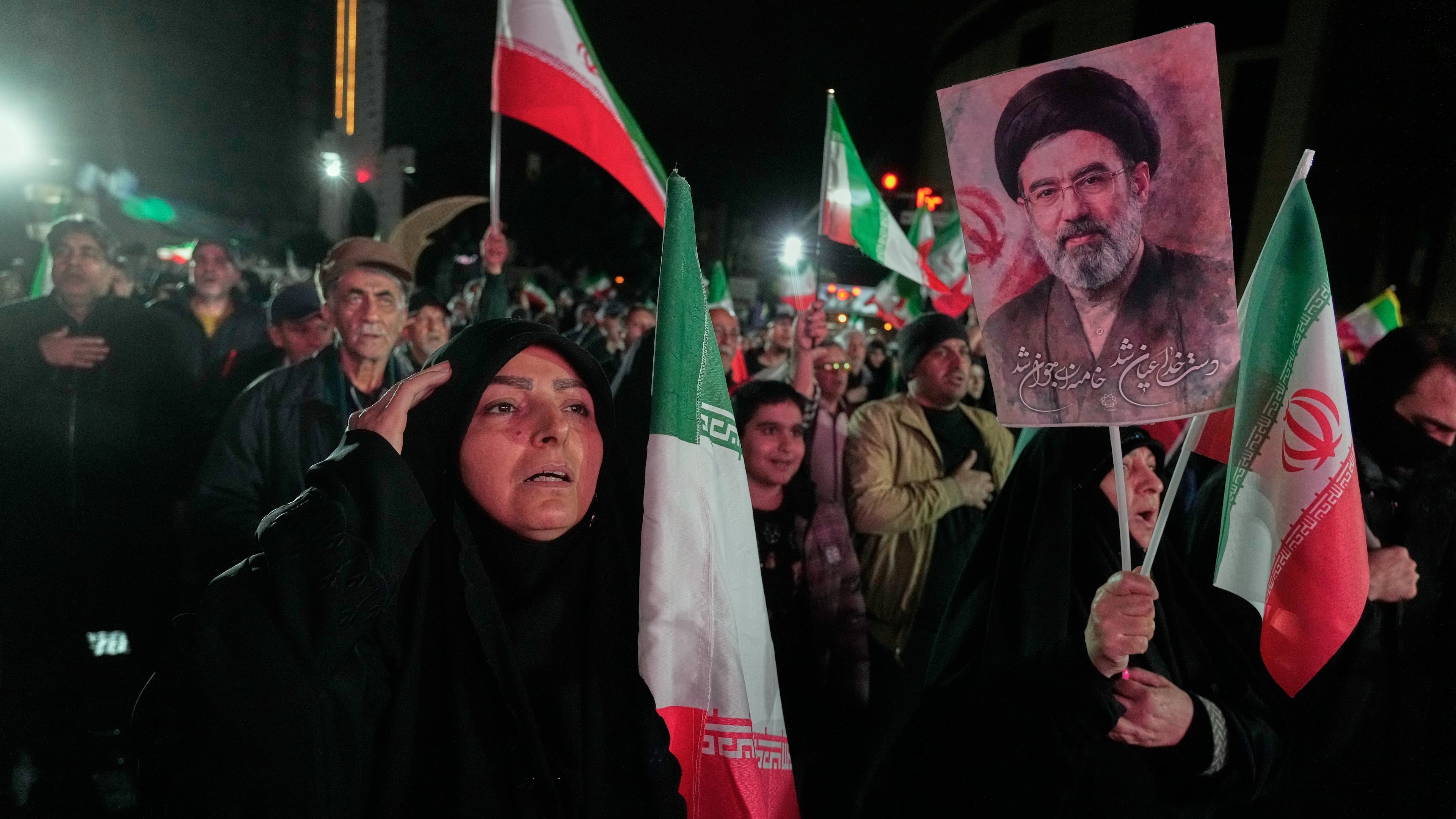 A woman salutes while singing the national anthem as another holds a picture of Iranian Supreme Leader Ayatollah Mojtaba Khamenei during a pro-government gathering in a square in western Tehran, Iran, Wednesday, March 25, 2026. (AP Photo/Vahid Salemi)
