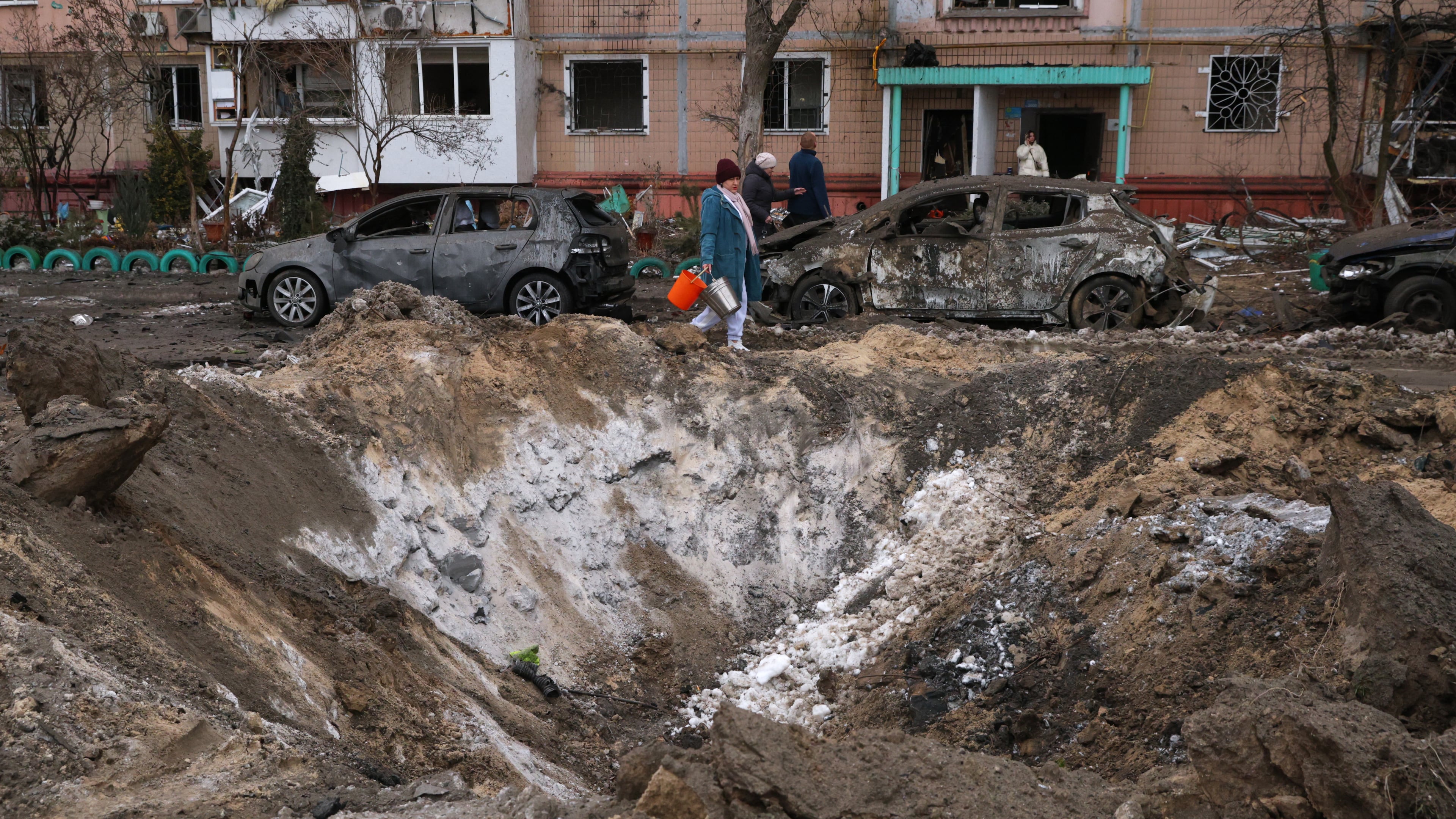 People pass a crater and damaged cars near an apartment building after a Russian attack in Zaporizhzhia, Ukraine, Wednesday, Jan. 28, 2026. (AP Photo/Kateryna Klochko)