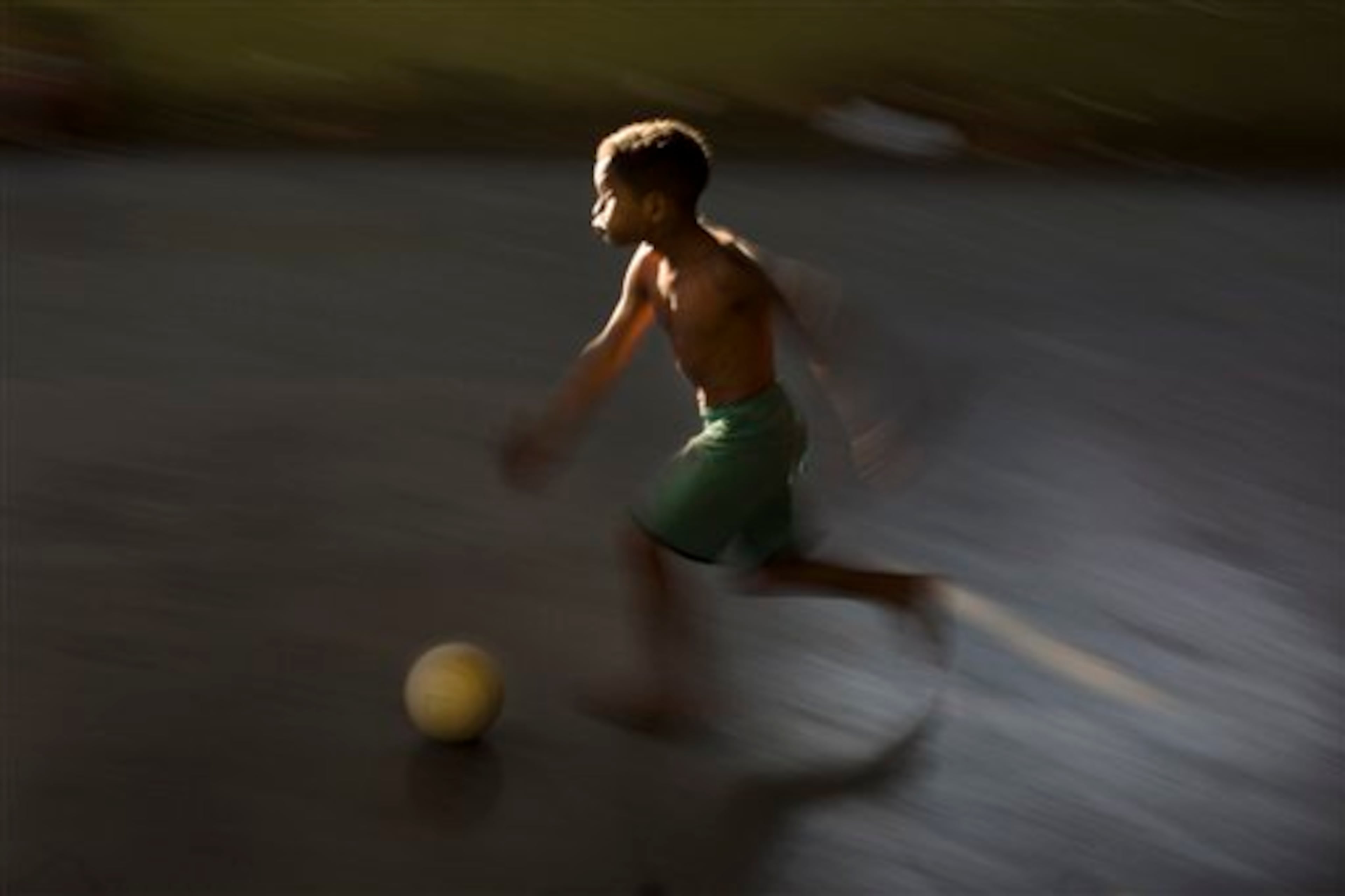 In this Monday, June 2, 2014, a youth runs with a soccer ball in a small court in the Mangueira slum of Rio de Janeiro, Brazil. The practical obstacles in accessing the Maracana stadium, located less than half a kilometer away, to watch World Cup games haven't dampened the boys' passion for what Brazilians call the "beautiful game." (AP Photo/Leo Correa)