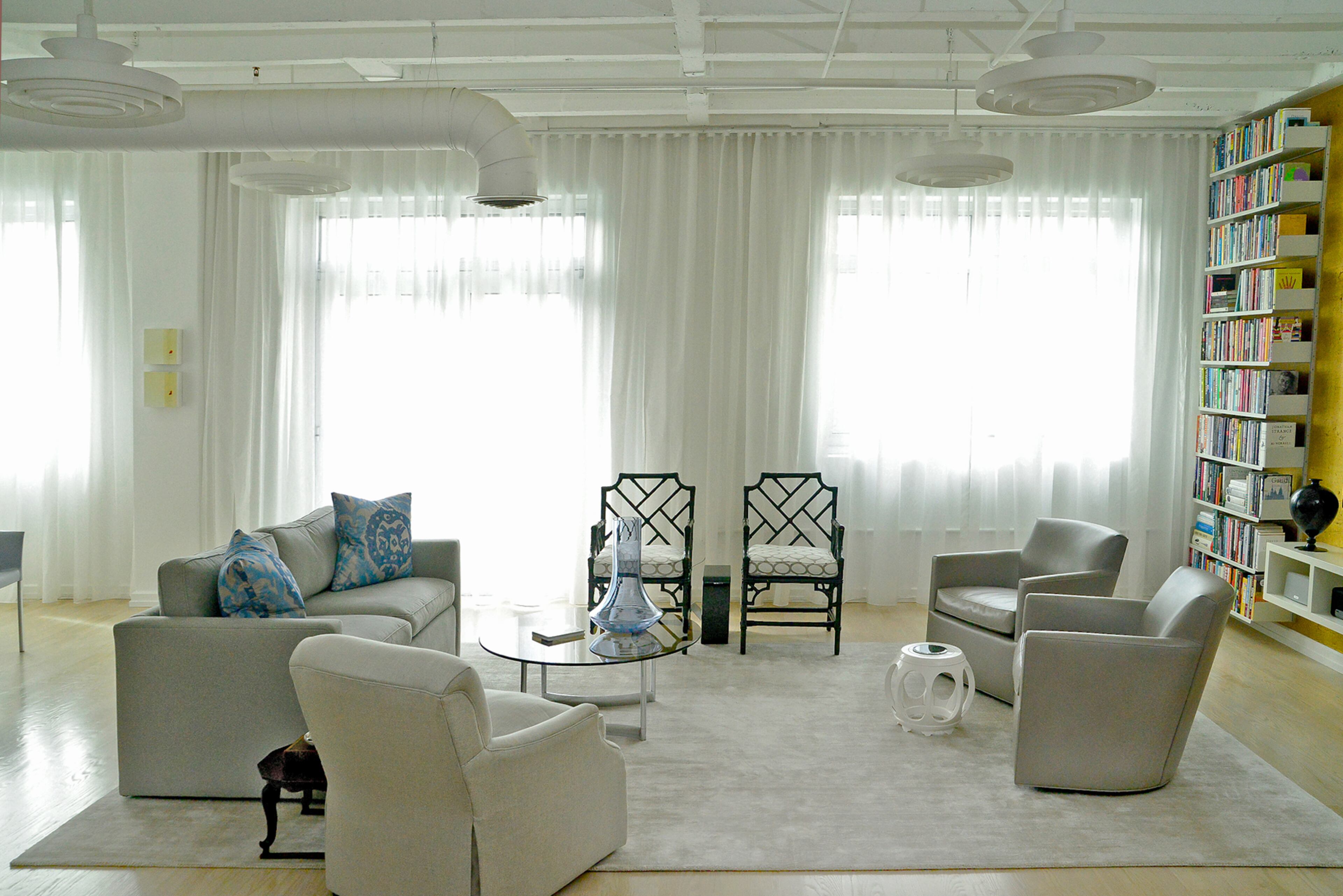 A wall of draperies, made of Sahco fabric, softens the condo's loft-style design in the living room, which opens to the dining area and kitchen. Underneath the TV, the media ledge was custom designed by homeowner Robert Gaul and fabricated by Long's Custom Trim & Cabinets. The vintage pendant lights are from a childhood church, St. Jerome Catholic Church in Walbridge, Ohio.