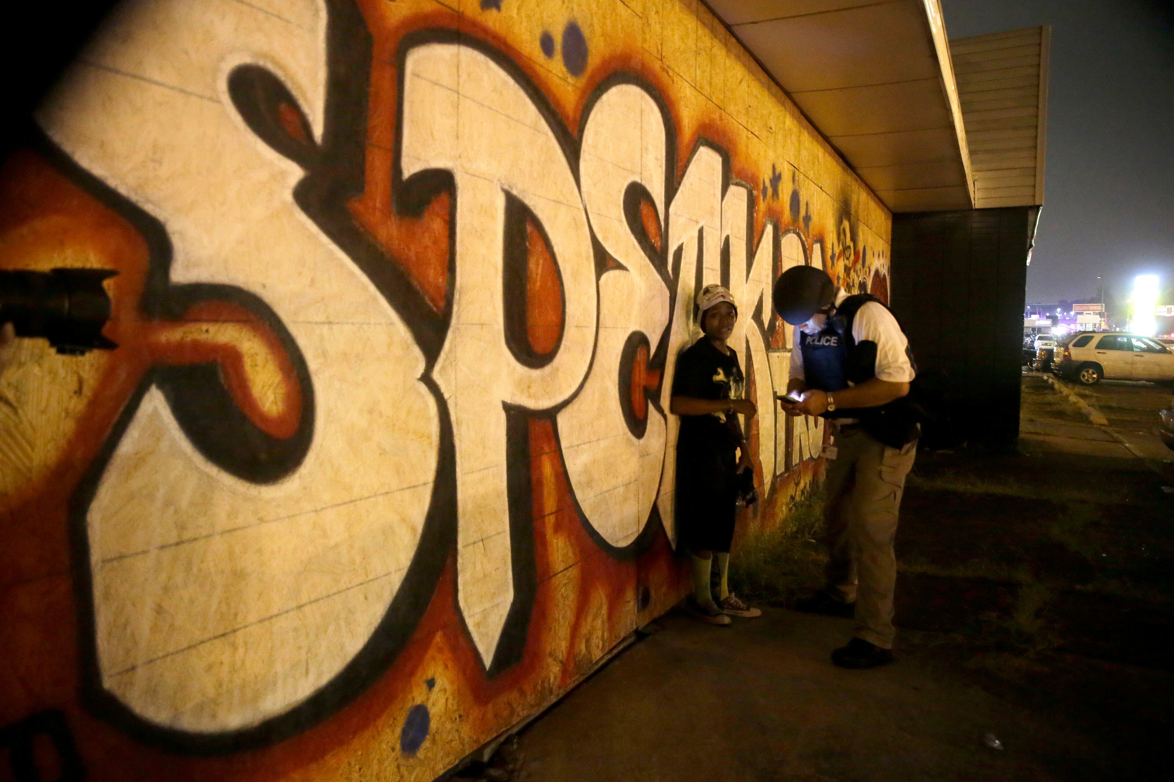 A police officer questions a person near the site of a shooting in Ferguson, Mo., Sunday, Aug. 9, 2015. The one-year anniversary of Michael Brown's death in Ferguson began with a march in his honor and ended with a protest that was interrupted by gunfire. (AP Photo/Jeff Roberson)