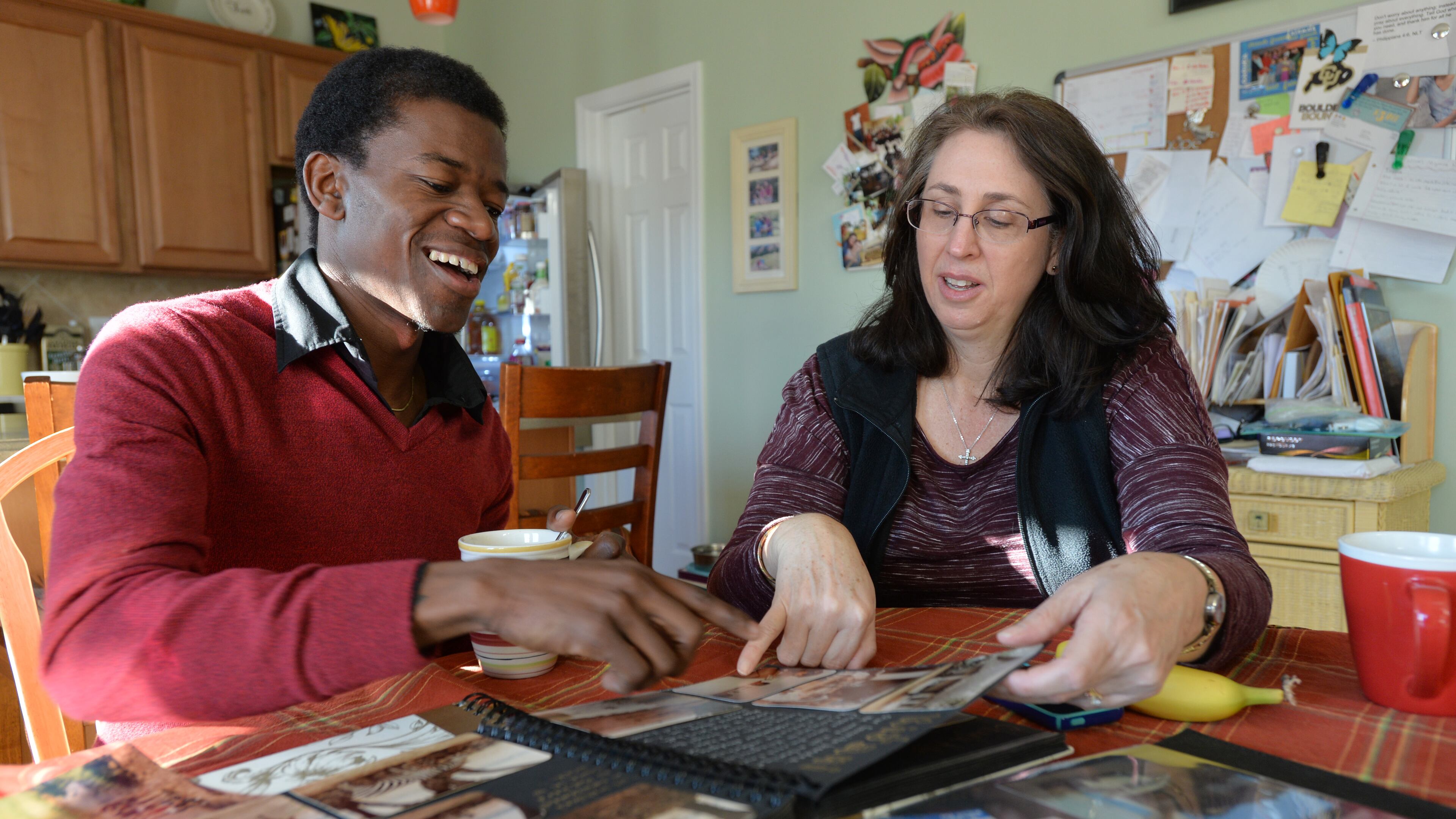 November 22, 2014 Woodstock - Samuel Johnson (left) reacts as Teresa Cook shows her family photos from Kenya while they have a tea time together at Teresa's home, where Samuel and his wife Mary Thompson stay, on Saturday, November 22, 2014. Personal Journey : Samuel Johnson was angry and swore vengeance on the men who killed his father during the civil war in Liberia. But his mother, a very spiritual woman, warned him against such action. Hatred only hurts you, she told her son. If you stop hating and think about how you can help people, blessings will flow. And, indeed, they have. Johnson found an number of "adoptive" families here in the United States, who have offered him shelter, a loving church family and in a project dear to his heart helped in help those still living in Guinea. Johnson was urged to leave when Ebola decimated parts of West Africa, but he vows to go back to help the many kids there he befriended. HYOSUB SHIN / HSHIN@AJC.COM