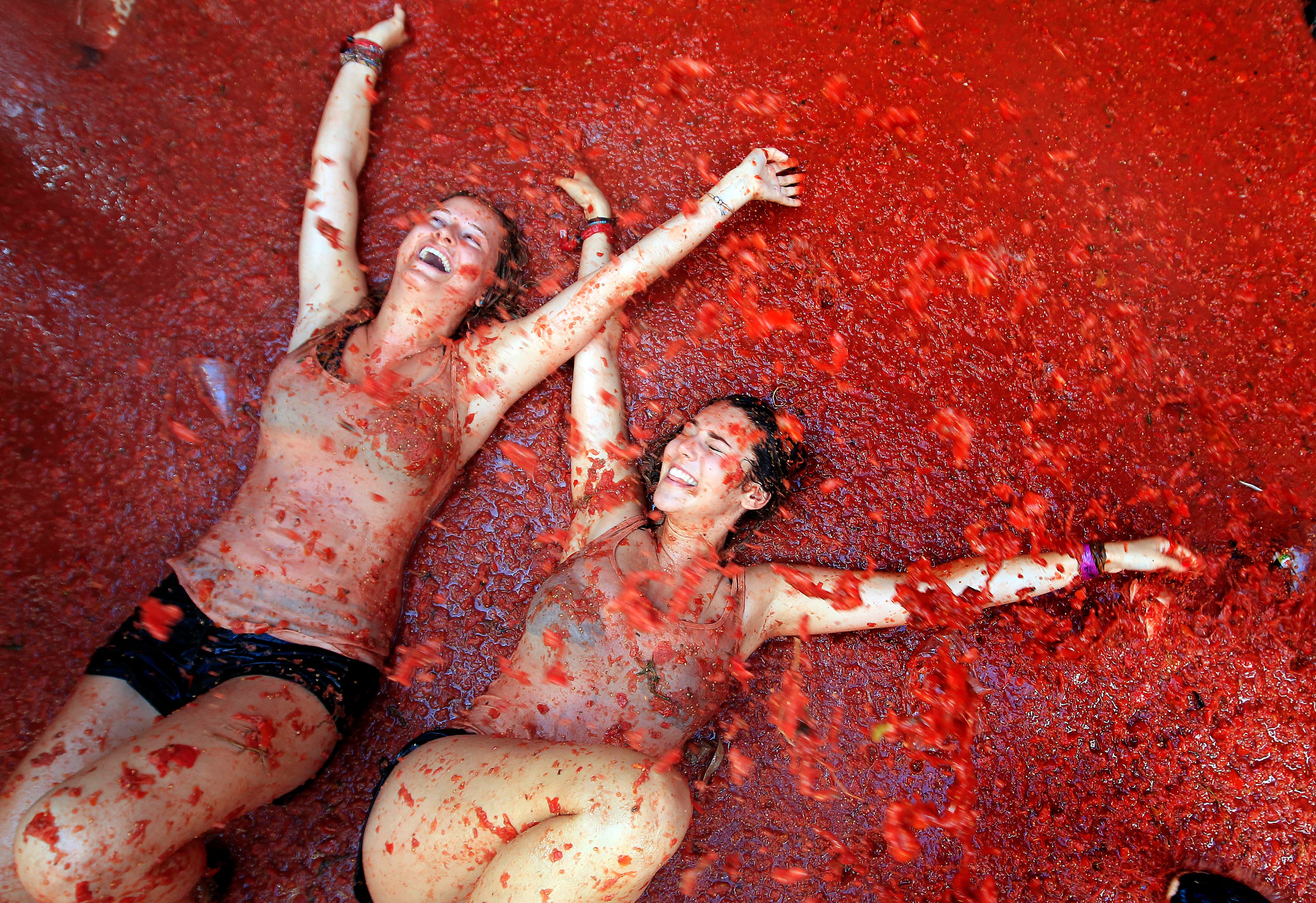 Two woman lie in a puddle of squashed tomatoes during the annual "tomatina" tomato fight fiesta, in the village of Bunol, 50 kilometers outside Valencia, Spain, Wednesday, Aug. 26, 2015. The streets of an eastern Spanish town are awash with red pulp as thousands of people pelt each other with tomatoes in the annual "Tomatina" battle that has become a major tourist attraction. At the annual fiesta in Bunol on Wednesday, trucks dumped 150 tons of ripe tomatoes for some 22,000 participants, many from abroad to throw during the hour-long morning festivities.