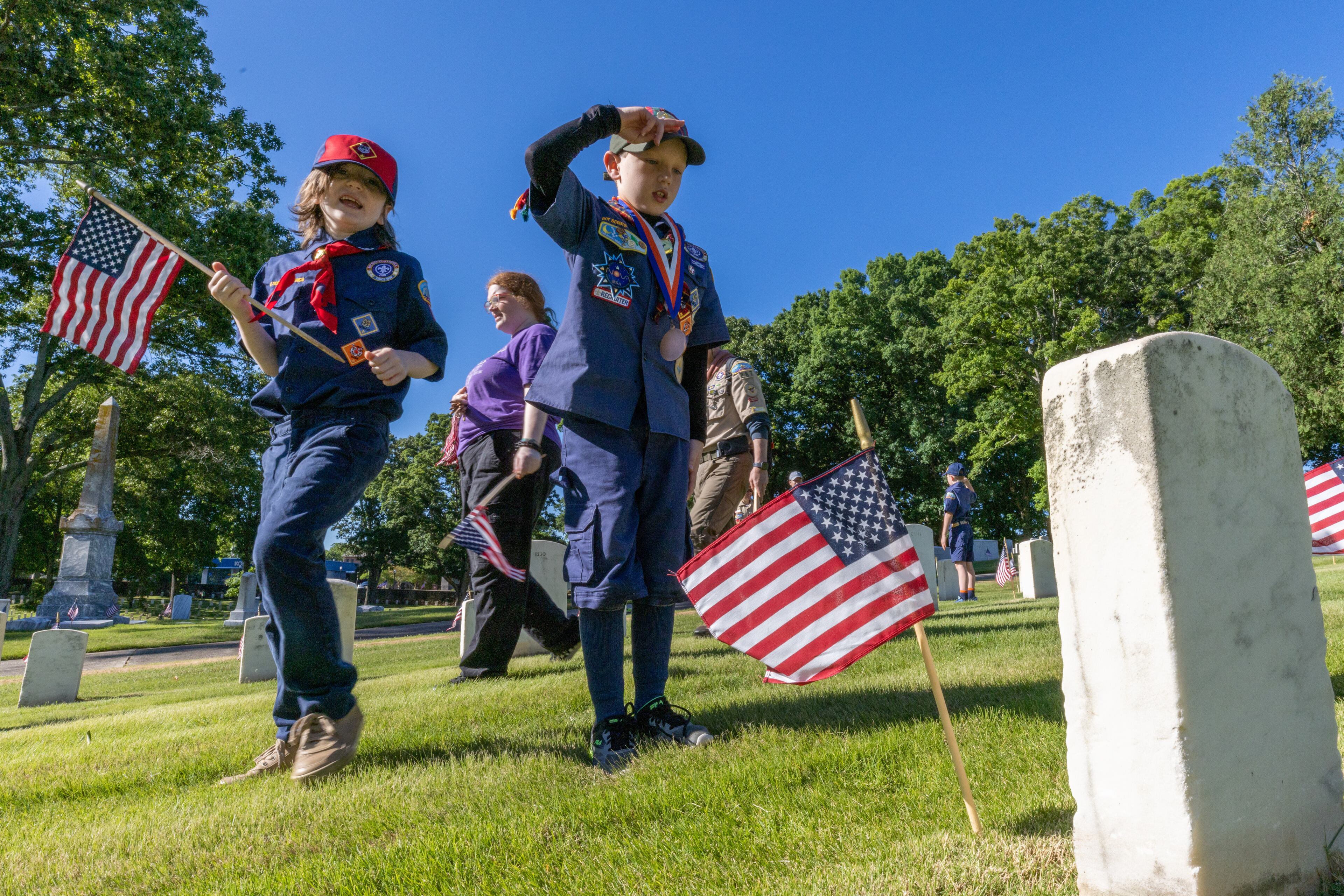 Alec Mayhan, 9, salutes after placing one of the over 18,000 flags in front of a tombstone at Marietta national cemetery Saturday, May 28, 2022. The flags are planted in front of all the tombstones in preparation for the Memorial Day ceremony Monday. (Steve Schaefer / steve.schaefer@ajc.com