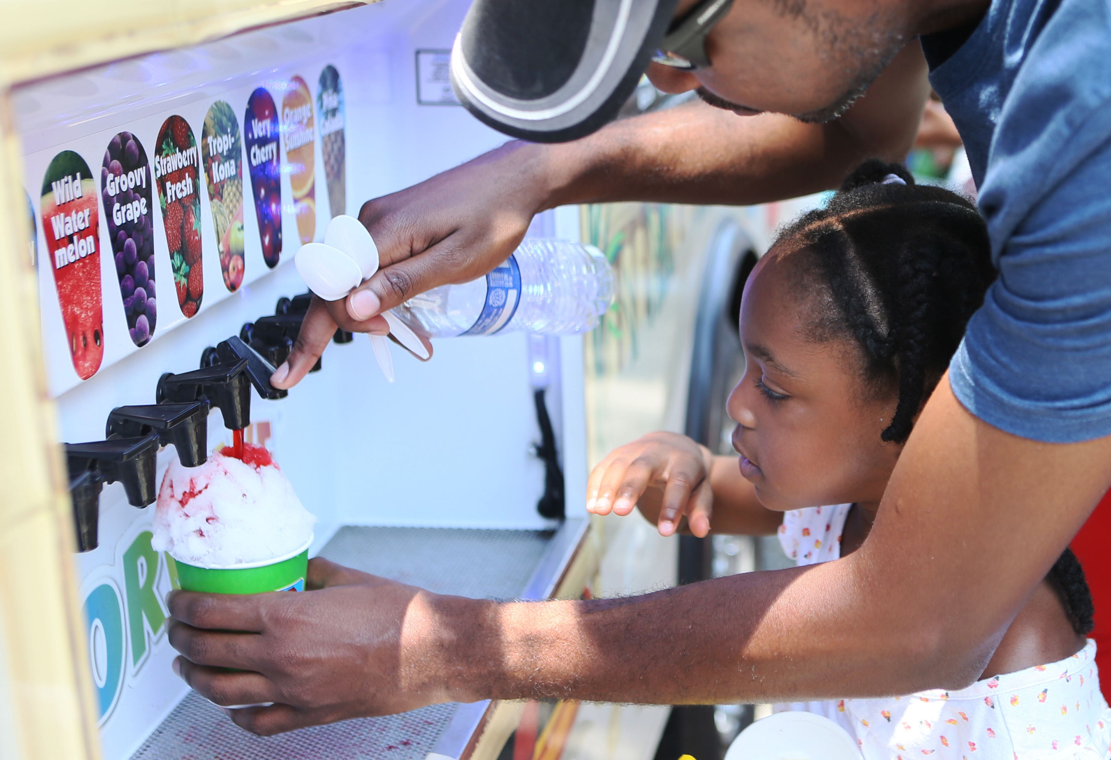 Griffith James helped his five-year-old daughter Kelci add flavoring to her Kona Ice as local artisans and national classics presented their best products at the 4th Annual Atlanta Ice Cream Festival at Piedmont Park in Atlanta on Saturday, July 26, 2014. There was a variety of health /wellness agencies, fitness routines, vendors, entertainment, bands and fun family activities. (Photo by Phil Skinner)