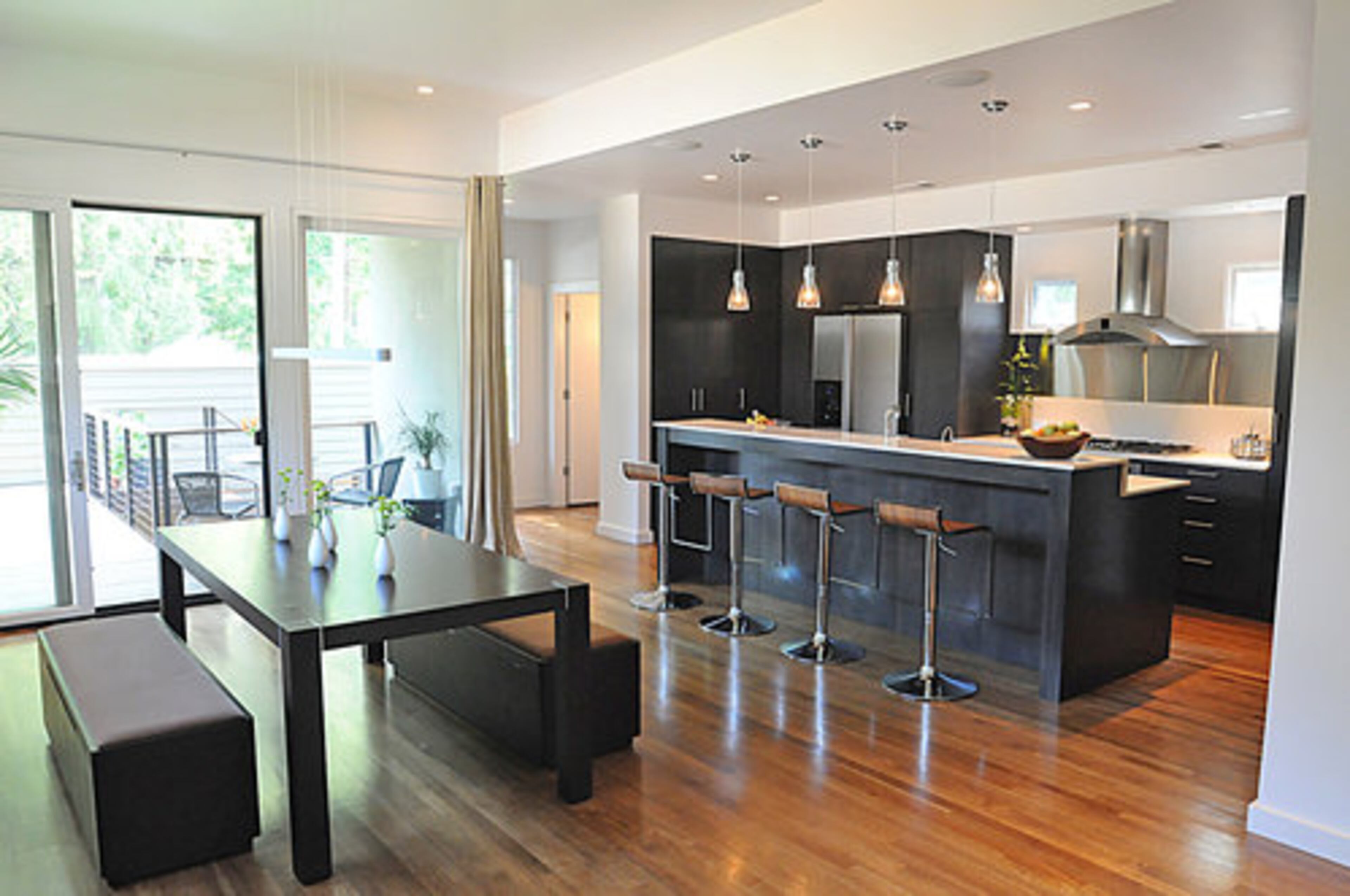 The home's floor plan is open and flowing. From the living room one can easily transition to the kitchen, which features four minimalist barstools perfect for a quick snack or a cocktail before dinner. The handsome dining table looks out on the home's lush outdoor area and the sliding doors can be opened to allow easy access for guests during dinner parties and other gatherings.