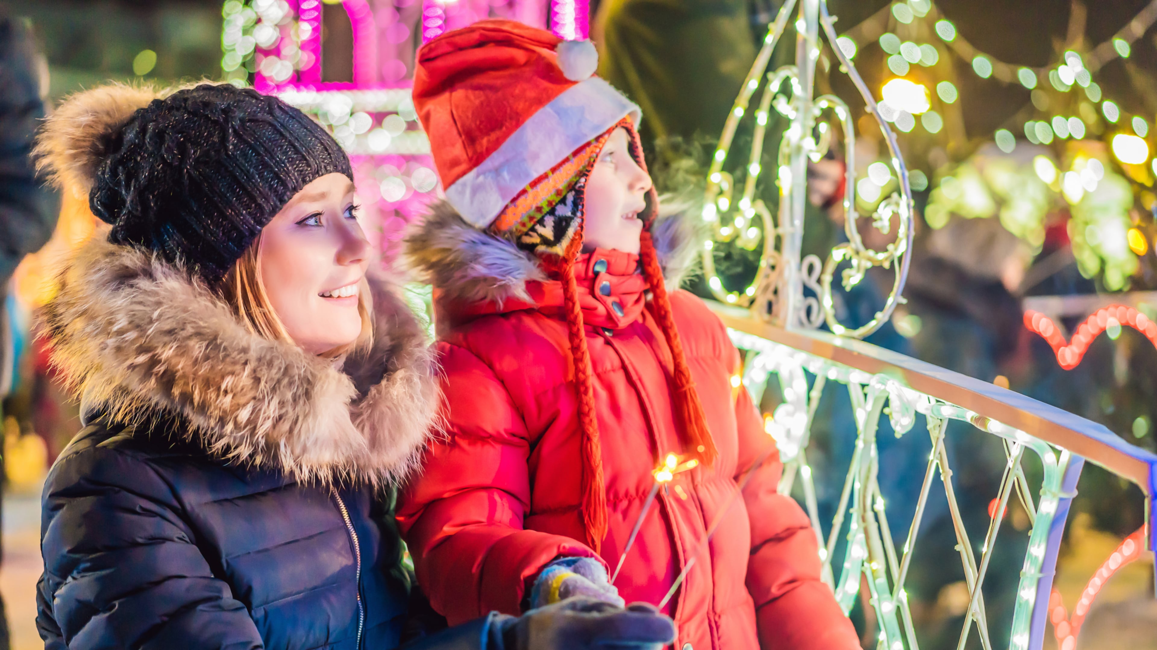 Little boy and his mother with sparklers near giant fir tree and Christmas illumination on Christmas market. Xmas holidays on fair.