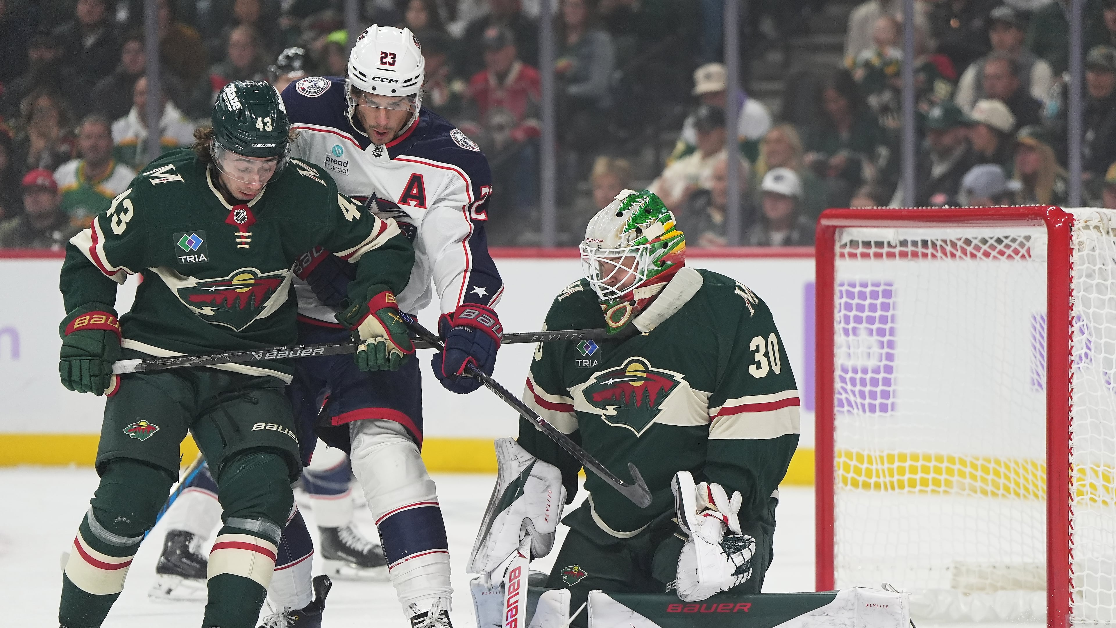 Minnesota Wild goaltender Jesper Wallstedt (30) and defenseman Quinn Hughes (43) defend against a shot as Columbus Blue Jackets center Sean Monahan (23) pressures them during the first period of an NHL hockey game, Sunday, Oct. 18, 2026, in St. Paul, Minn. (AP Photo/Abbie Parr)