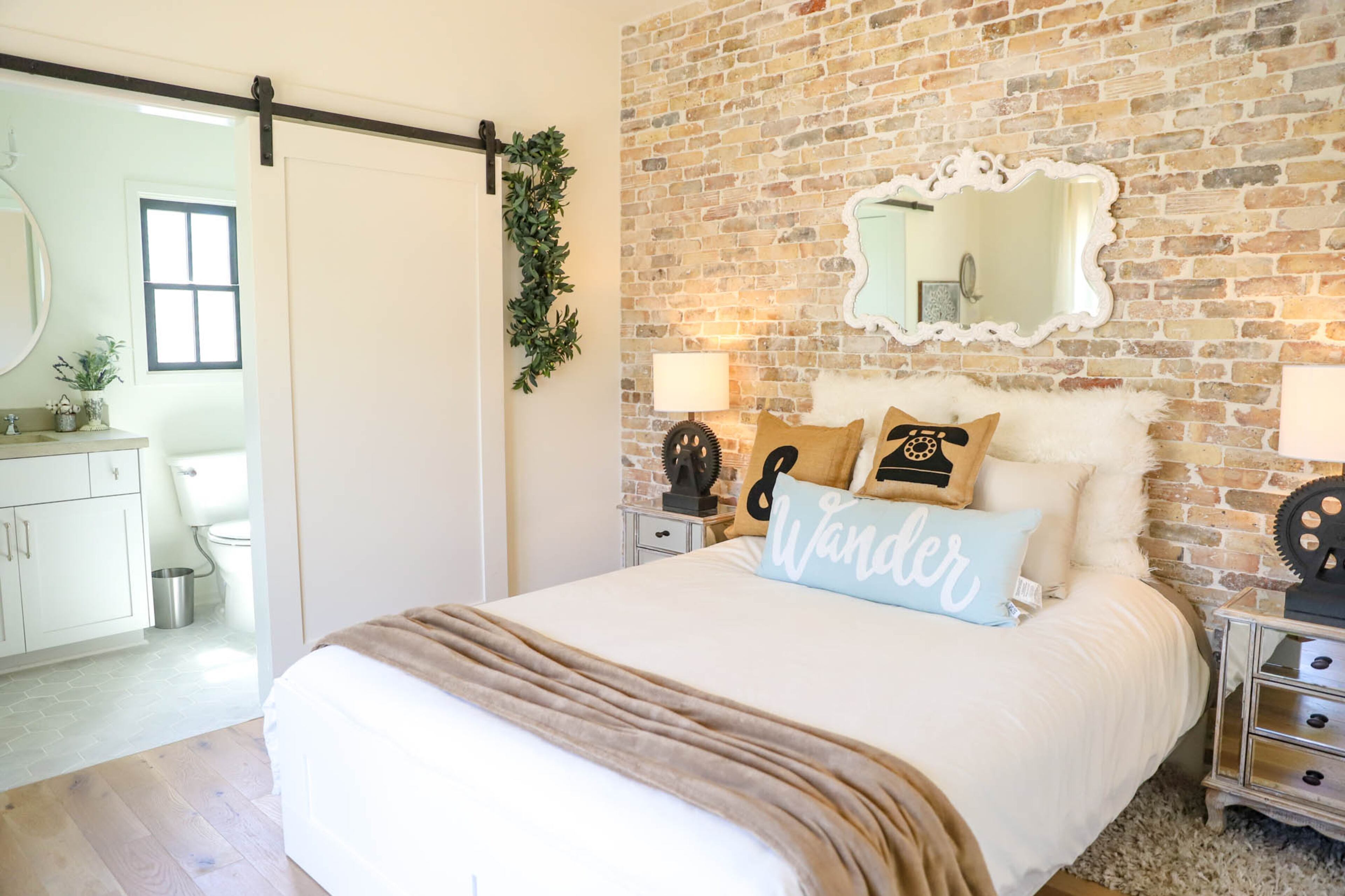 Mimi Tin's goal with the second bedroom was to inspire creativity in anyone who stayed there. The burlap pillows, made by Tin, provide texture and a vintage look that complements the brick accent wall. A sliding door and the mirror above the headboard help maximize the space.