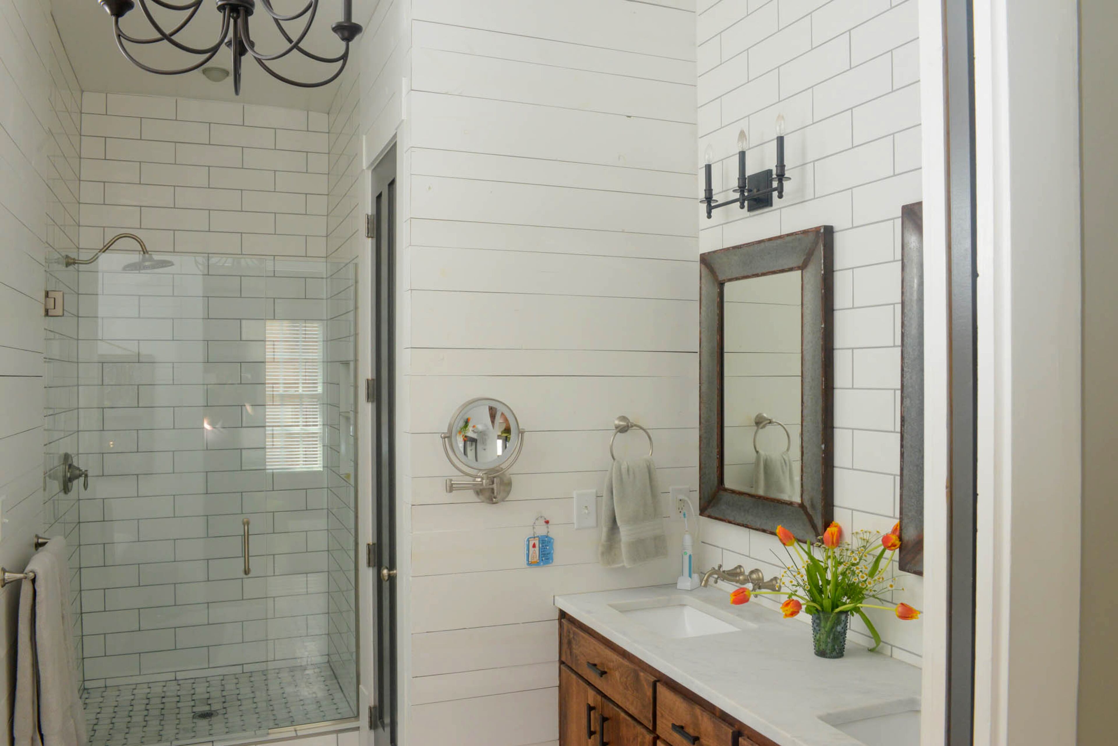 The white subway tile found in the kitchen also made its way to the master bathroom. Elsewhere on the walls, she used boards of random widths, inspired by the walls elsewhere in the home. The chandelier is from Lamps Plus, mirrors from Ballard Designs and fixtures from Fergusons.