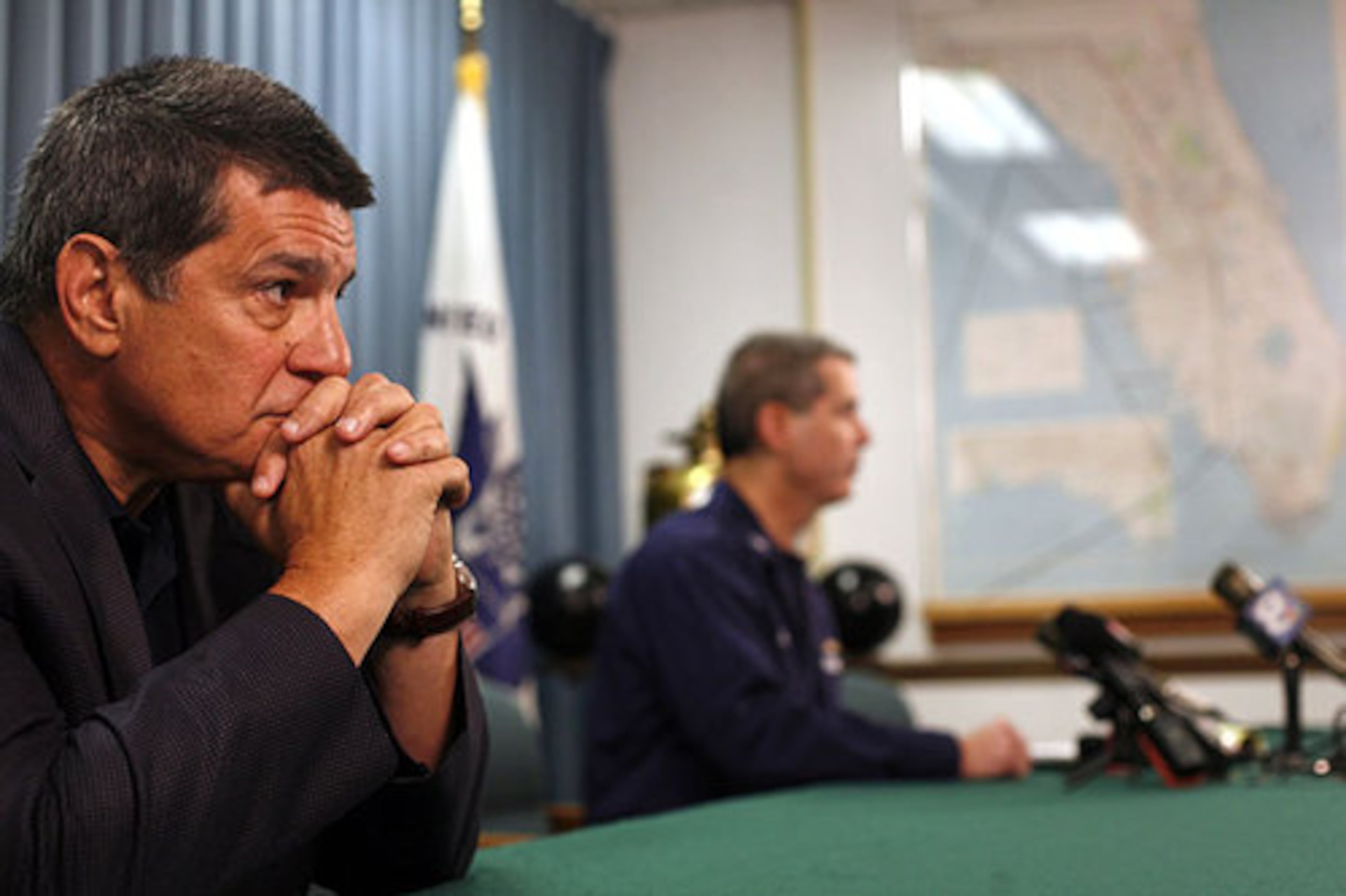 Dan Grossi (left) who works for the NFL's security division, listens as Coast Guard Capt. Timothy M. Close speaks to the media about the search for the missing boat March 1, 2009.