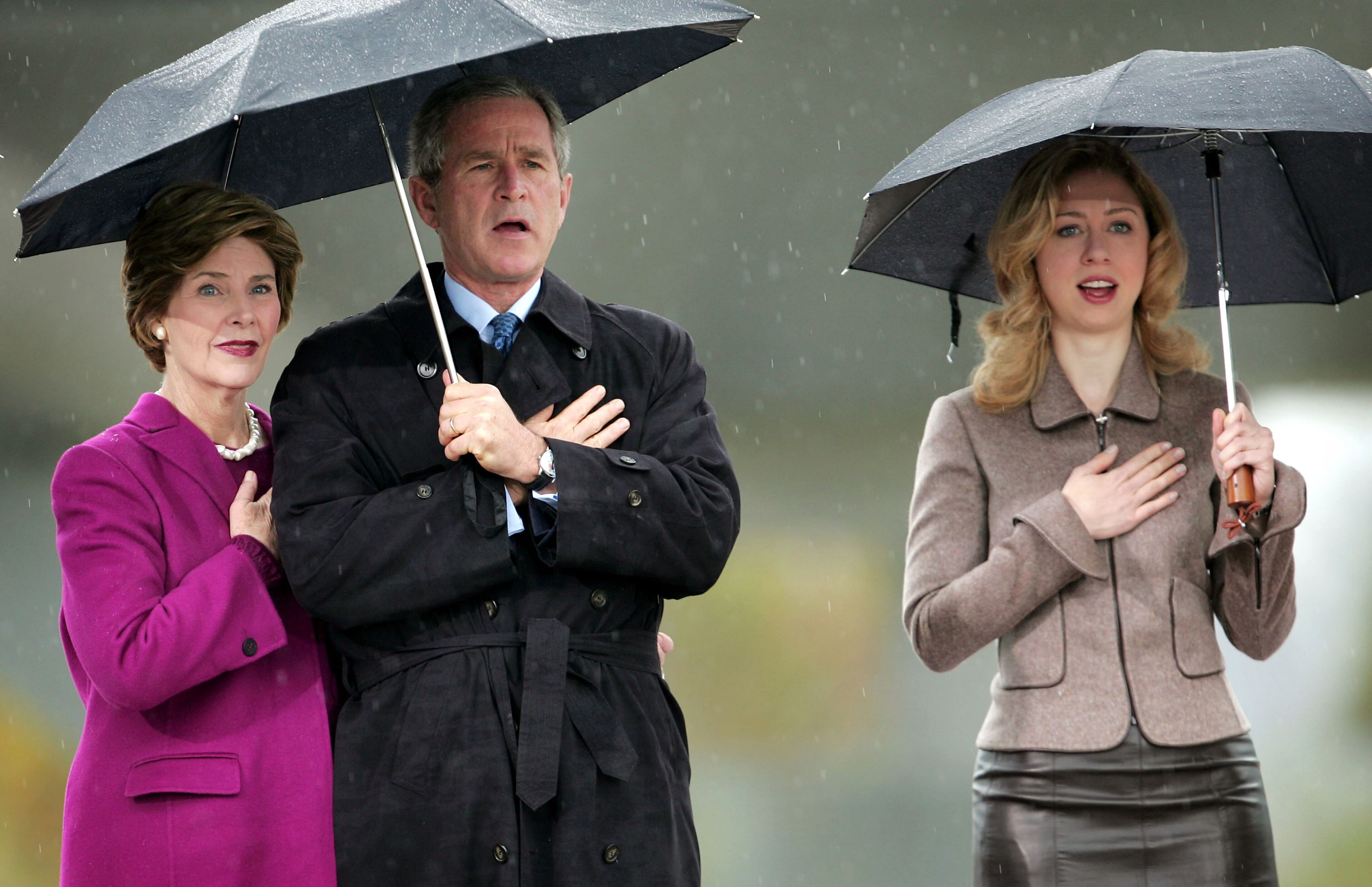 U.S. President George W. Bush (C), first lady Laura Bush (L), and daughter of former U.S. President Bill Clinton, Chelsea Clinton (R), sing the National Anthem at the dedication of the William J. Clinton Presidential Center November 18, 2004 in Little Rock, Arkansas. An estimated 30,000 spectators gathered in the rain on the grounds of the library to view the dedication of the $165 million facility. (Photo by Scott Olson/Getty Images)
