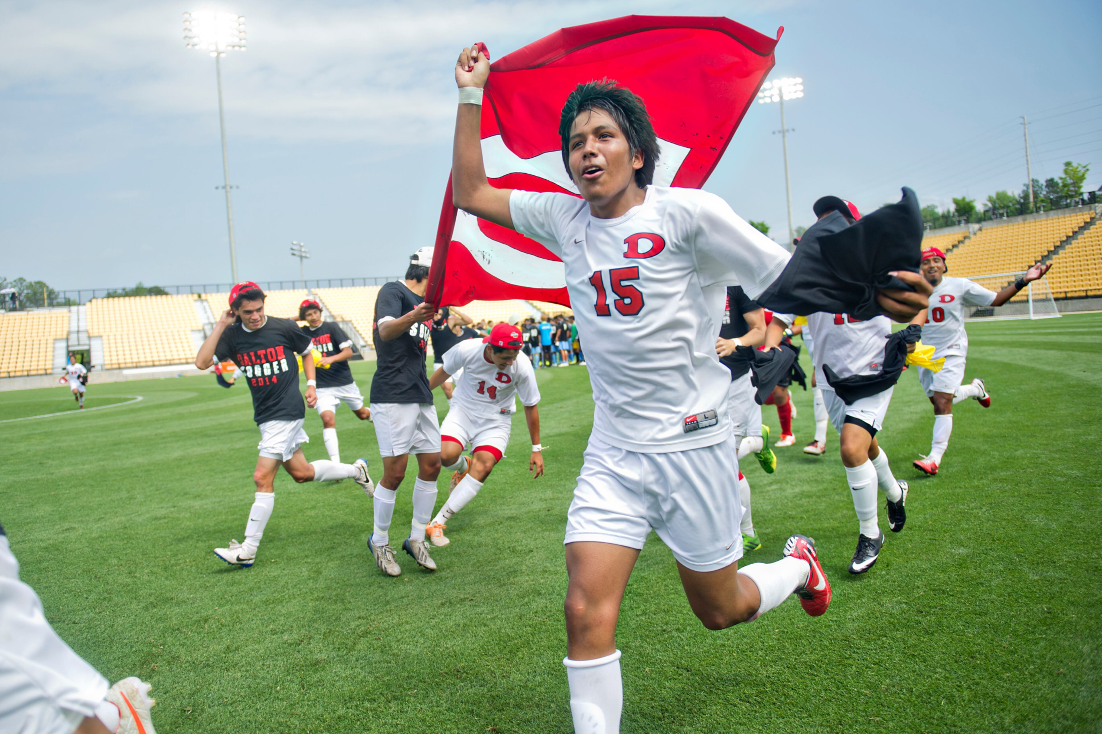Dalton's Edgar Hernandez (15) runs around the field carrying the Dalton High School flag after defeating Johnson 2-0 during the Class AAAA championship soccer game at Kennesaw State University on Saturday, May 17, 2014.