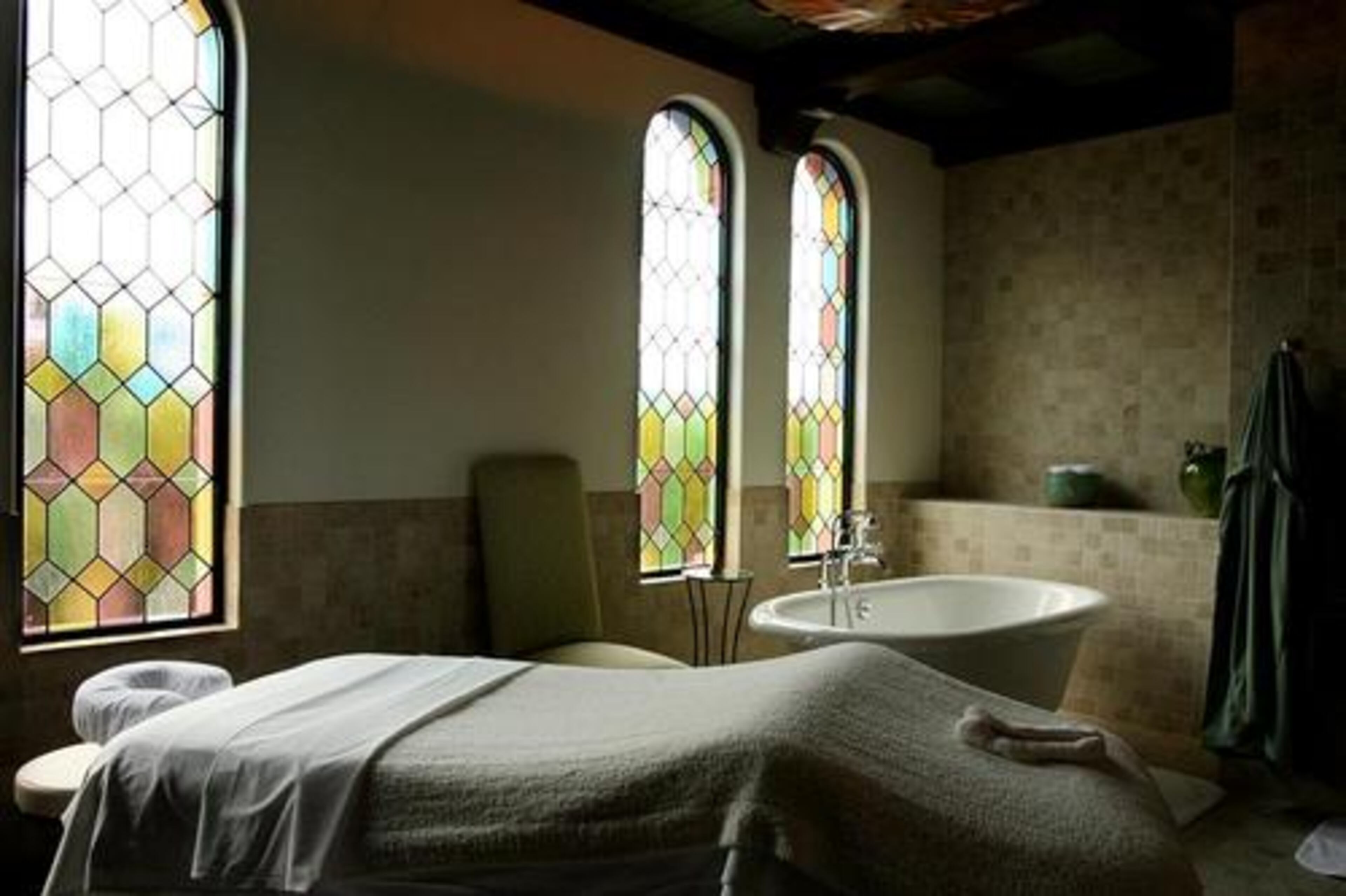 A treatment room at The Spa at Sea Island awaits a guest who will be pampered with luxuirant facials, massages and other treatments. The room features stained glass windows, a deep bath tub, and shower.