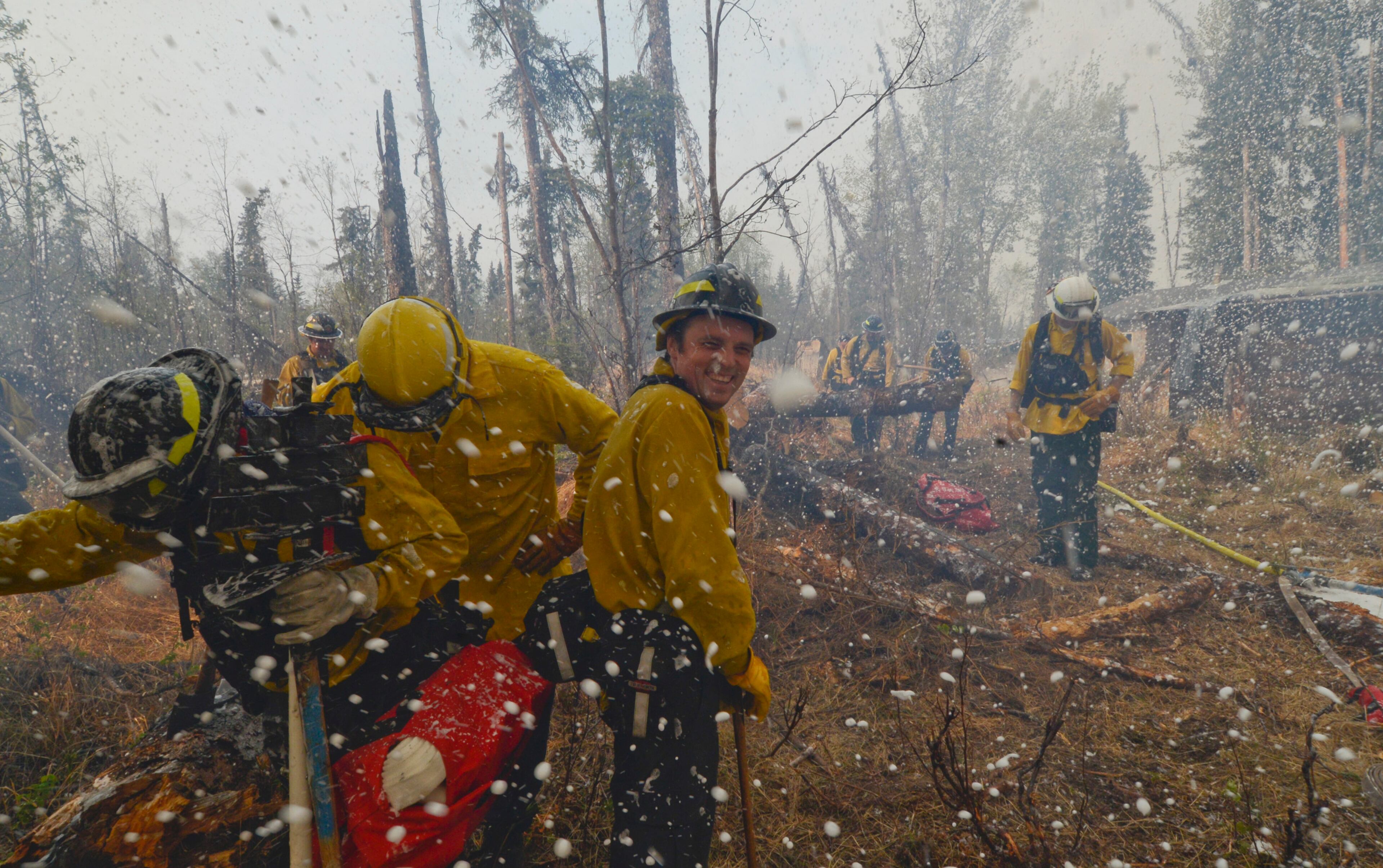 Central Emergency Services firefighter Terry Bookey, center, is showered with foam while fighting a wildfire Sunday, May 25, 2014, in the Funny River community in Soldotna, Alaska. A massive wildfire pushed by wind in Alaska's Kenai Peninsula south of Anchorage continued to explode in size, leading to mandatory evacuations of at least 1,000 structures, officials said Sunday. (AP Photo/Peninsula Clarion, Rashah McChesney)