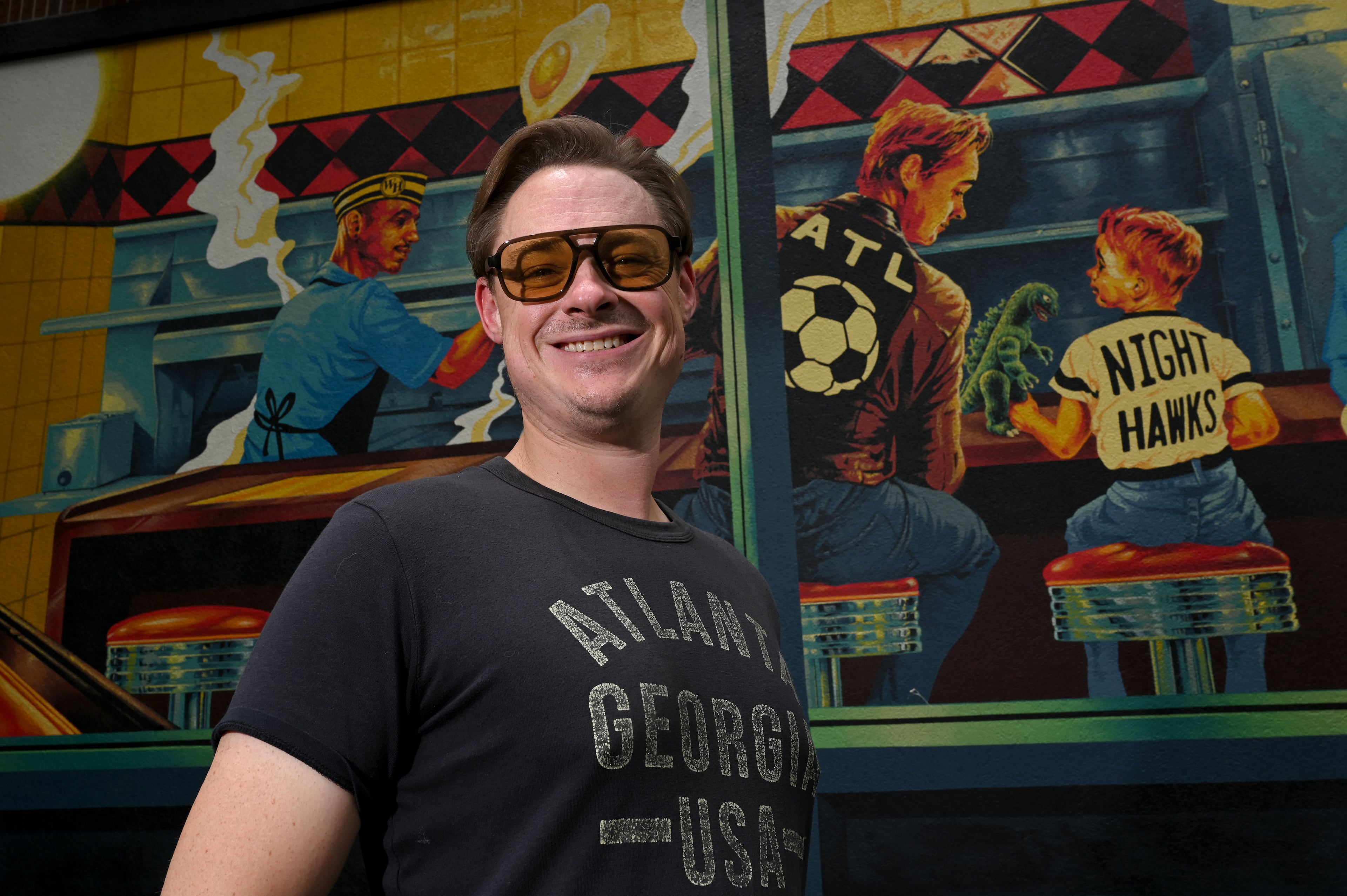 Artist Nick Benson poses for a portrait in front of his mural. He included a self portrait of himself in the style of Norman Rockwell's iconic painting, "The Runaway." (Hyosub Shin/AJC)