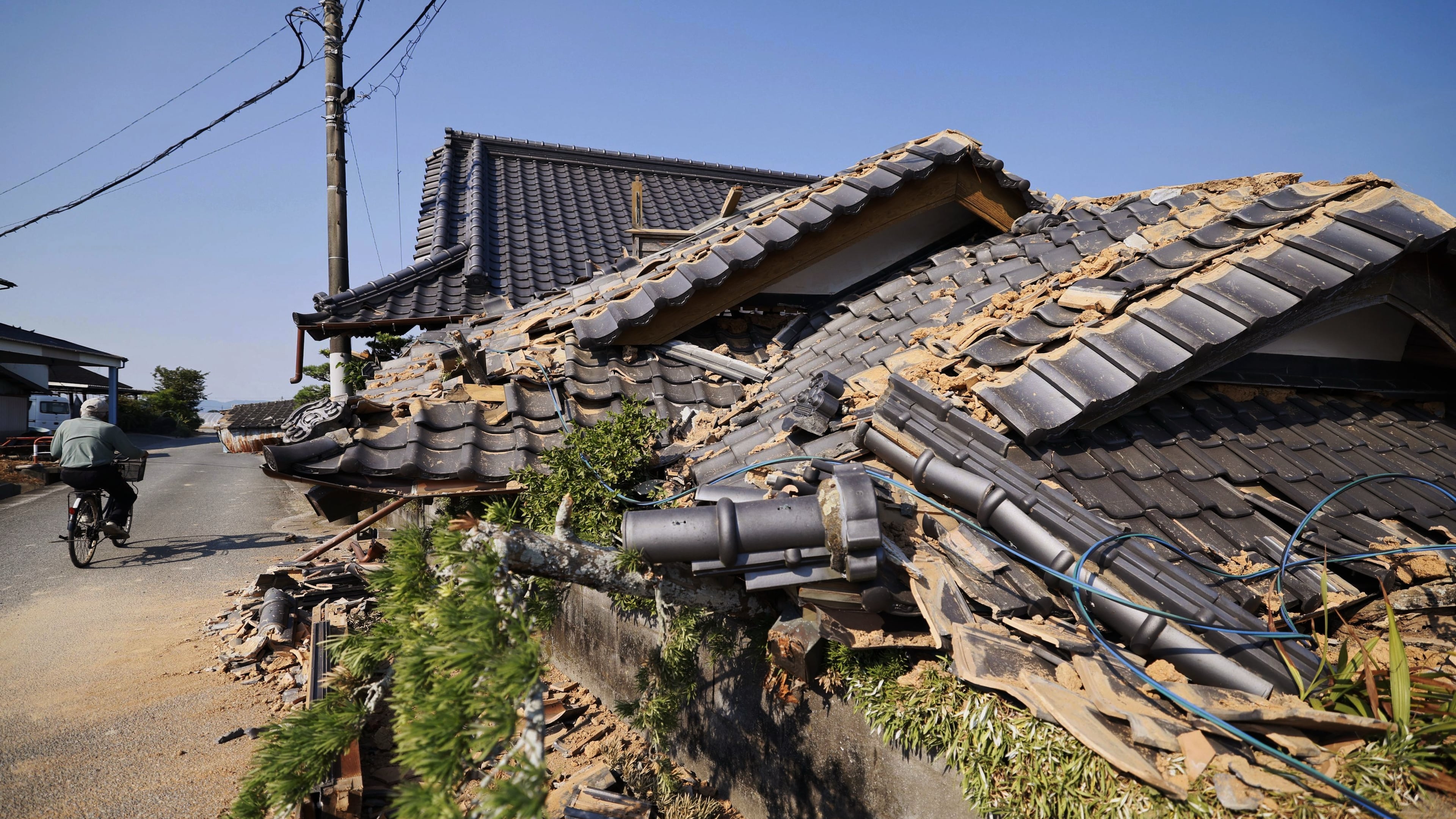 A person rides a bicycle past damaged buildings in Hikawa, southern Japan, Sunday, Aug. 2, 2026, following a July 28 earthquake. (Taichi Nagahisa/Kyodo News via AP)