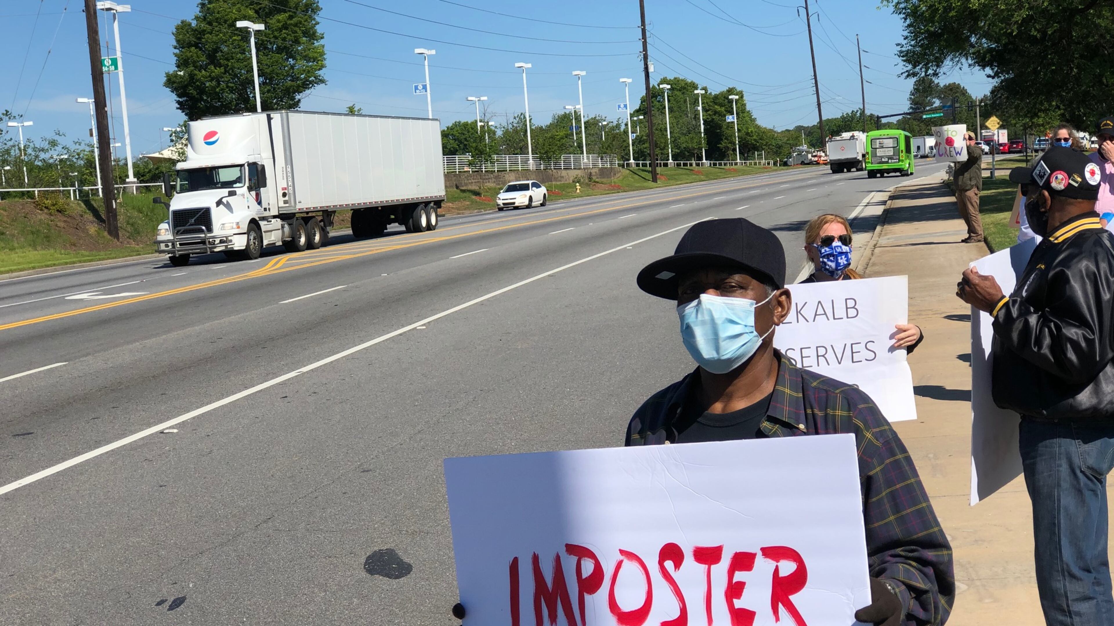 A protester holds a sign that reads "imposter" in red capital letters outside the DeKalb County School District headquarters on Mountain Industrial Boulevard in Stone Mountain on Friday, May 1, 2020. (MARLON A. WALKER/marlon.walker@ajc.com)