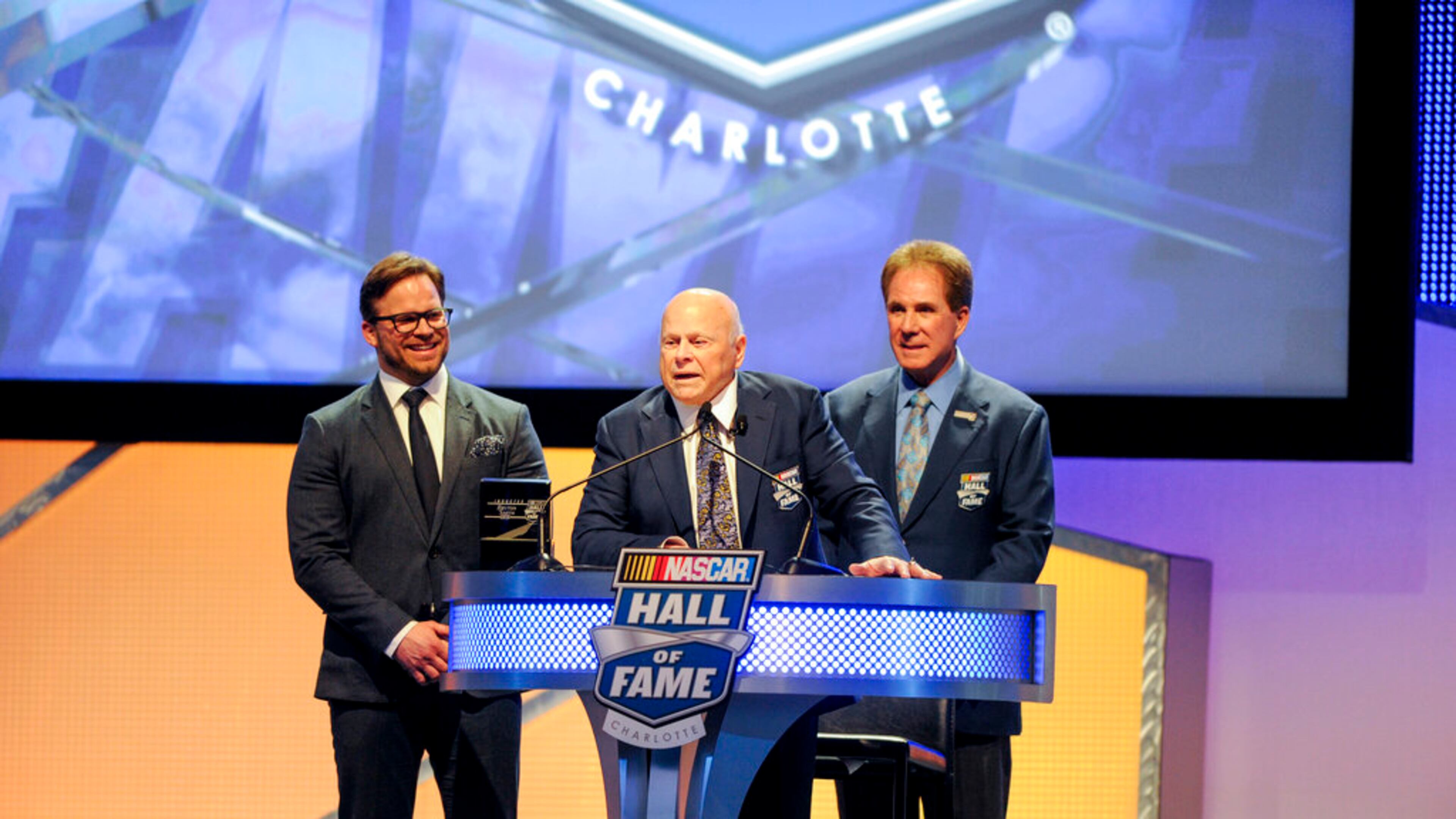 Hall of Fame inductee Bruton Smith, center entertains the crowd as his son, Marcus Smith, left and Hall of Fame member Darrell Waltrip, right look on during the NASCAR Hall of Fame Induction ceremony in Charlotte, N.C., Saturday, Jan. 23, 2016. (AP Photo/Mike McCarn)