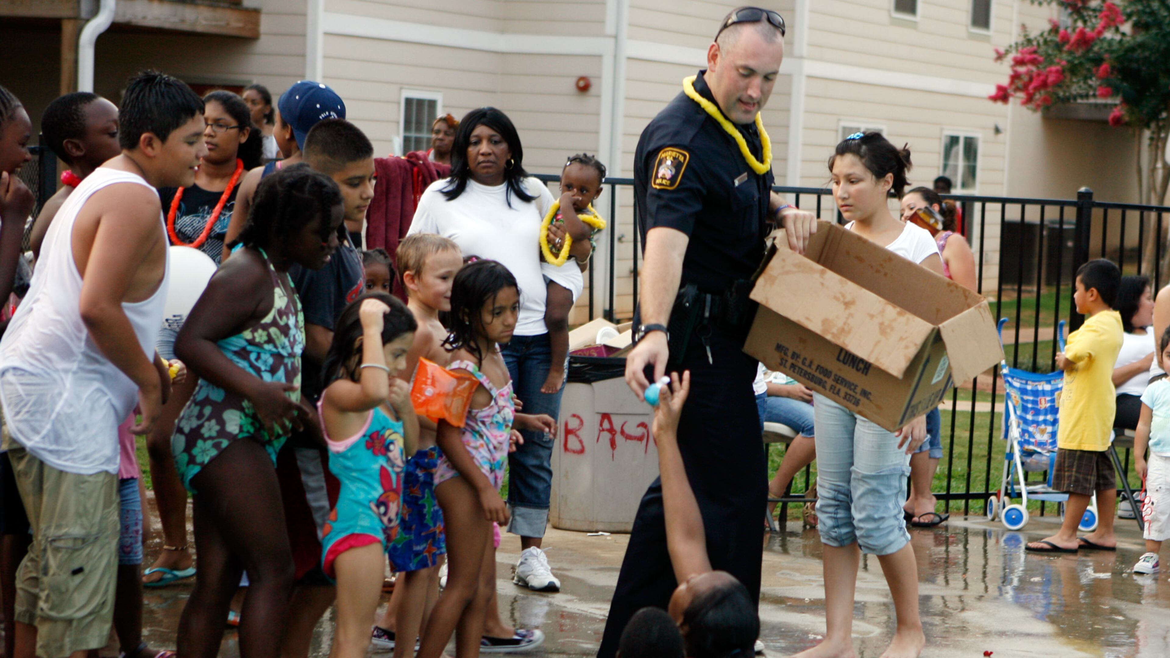 Followed by young Casa Mia Trace apartment residents eager for a toy prize, Marietta police officer Heath Henderson hands a ball to a mother and her child during National Night Out in 2010. AJC file photo.