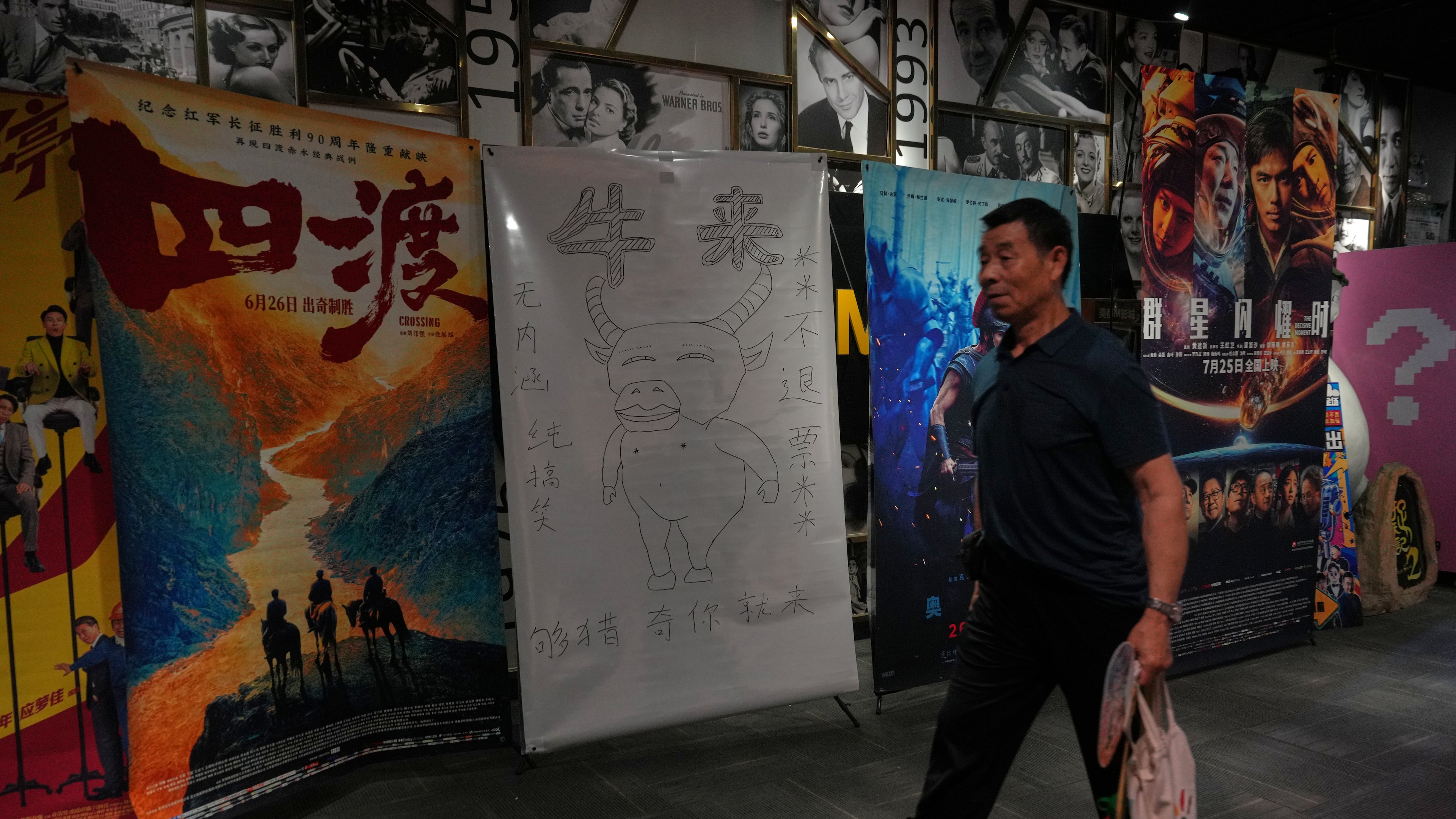 A man walks by a drawing poster promoting a Chinese animated film "Niulai" on display with other movie posters at a cinema in Beijing, Tuesday, Aug. 18, 2026. (AP Photo/Andy Wong)