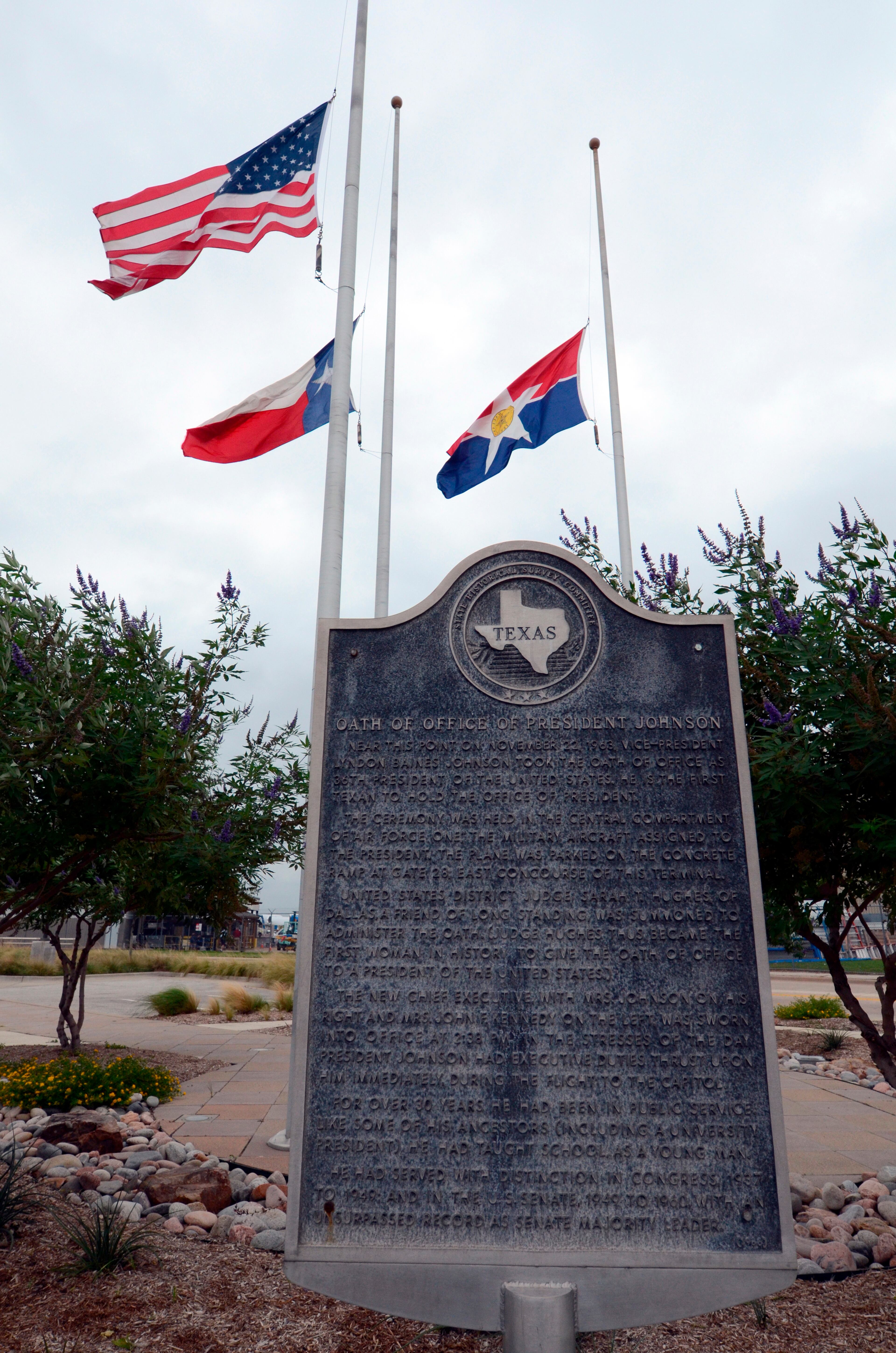 This photo taken in Dallas shows a historical plaque standing at Love Field which proclaims that Lyndon B. Johnson took the oath of office at the airport on Nov. 22, 1963, following the assassination of President John F. Kennedy. Flags in background were flying half staff by order of President Obama after the passing of former Speaker of the House Thomas S. Foley. (AP Photo/Benny Snyder)