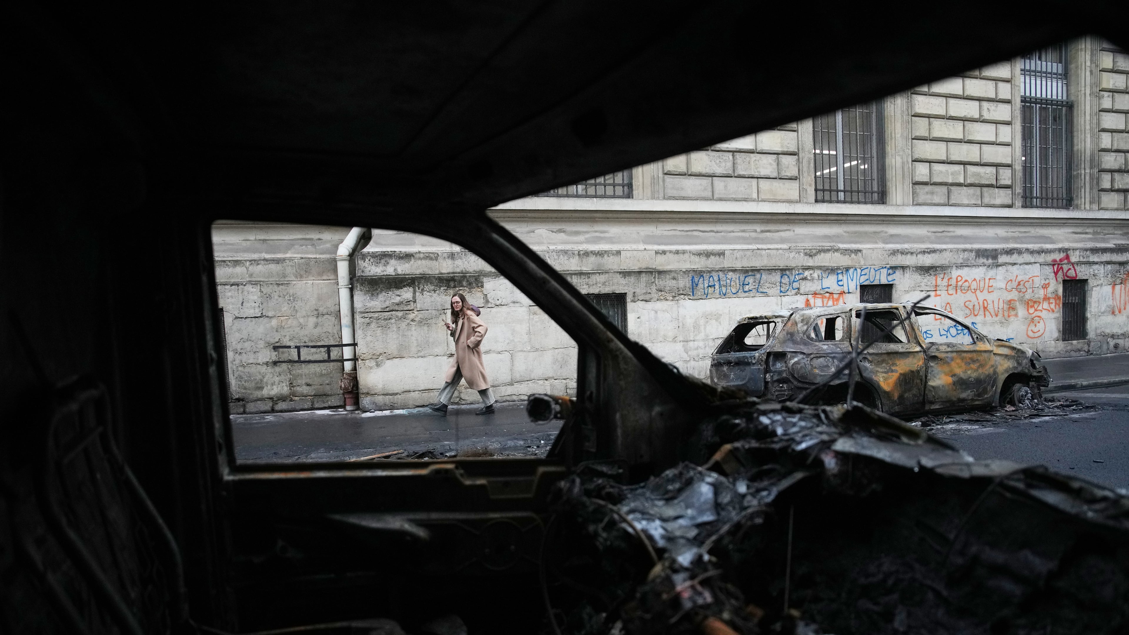 A woman walks past burned-out cars after a quiet night Monday under curfew, the first since weekend protests over the cost of living turned into rioting and looting across France, in Paris, Tuesday, Oct. 20, 2026. (AP Photo/Christophe Ena)
