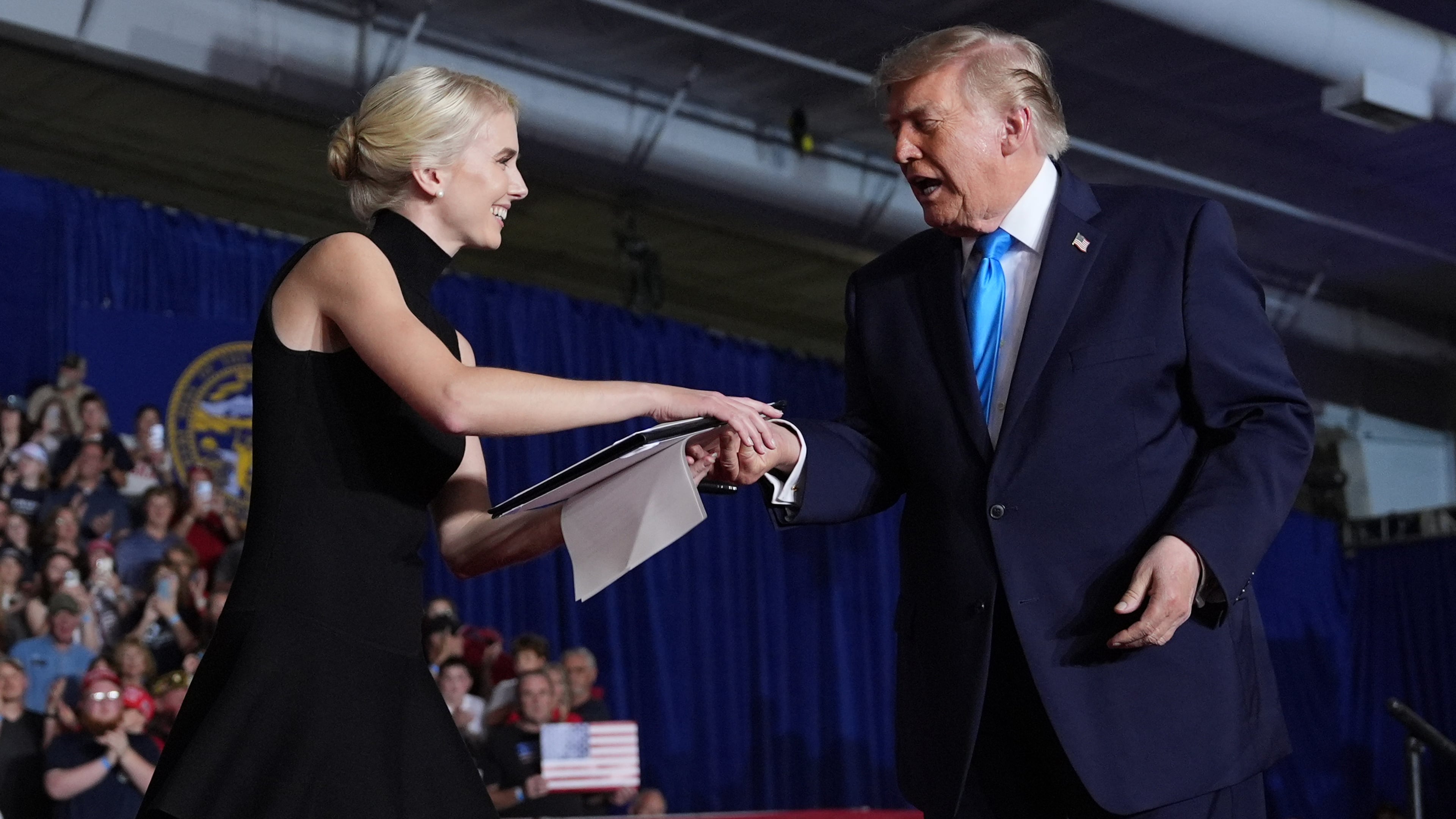 President Donald Trump hands a signed executive order to White House aide Natalie Harp at a campaign rally at the Pinnacle Bank Expo Center, Monday, Oct. 5, 2026, in Grand Island, Neb. (AP Photo/Alex Brandon)