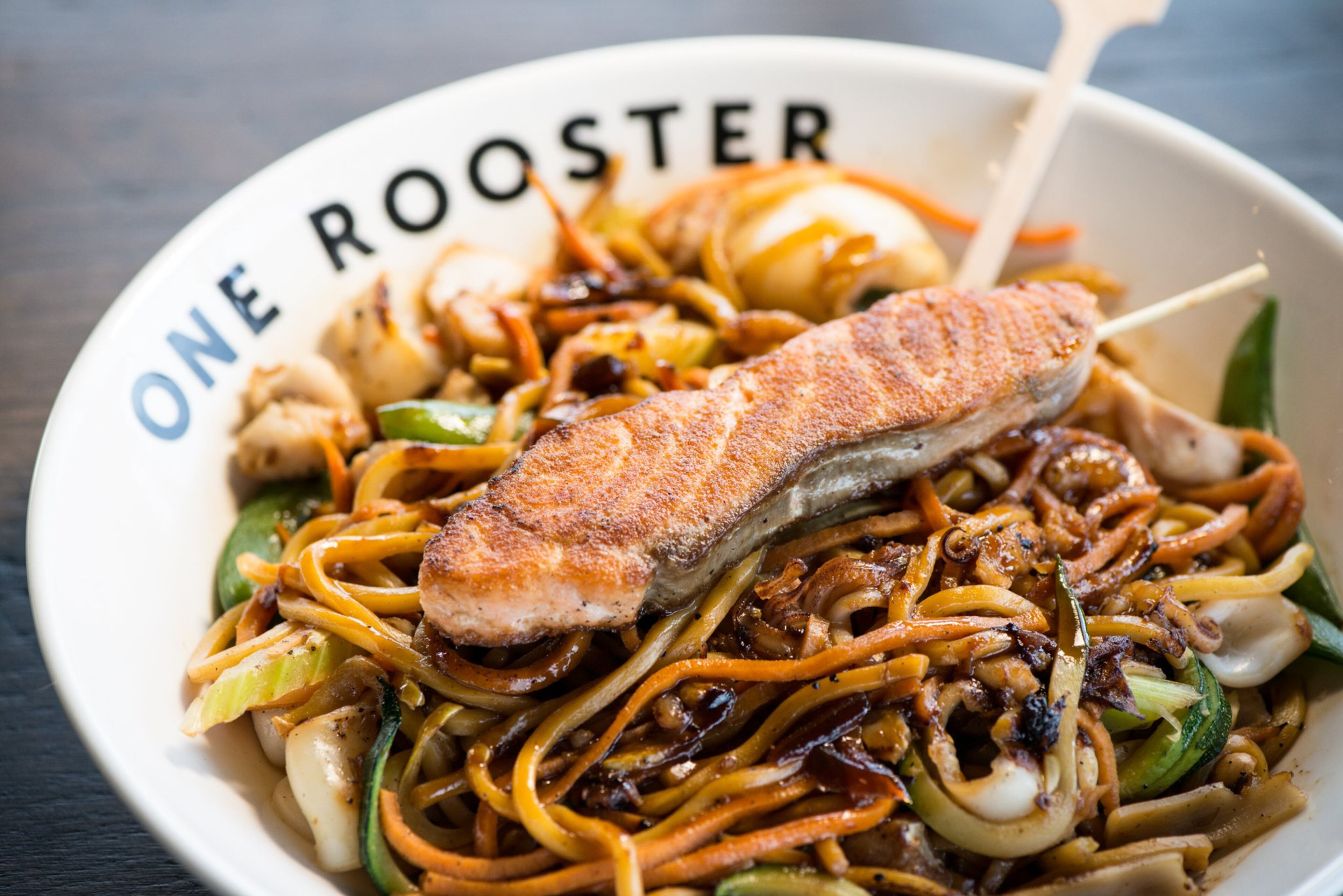 One Rooster Lo Mein bowl with calamari, veggies, ginger teriyaki sauce, and seared salmon. Photo credit - Mia Yakel.