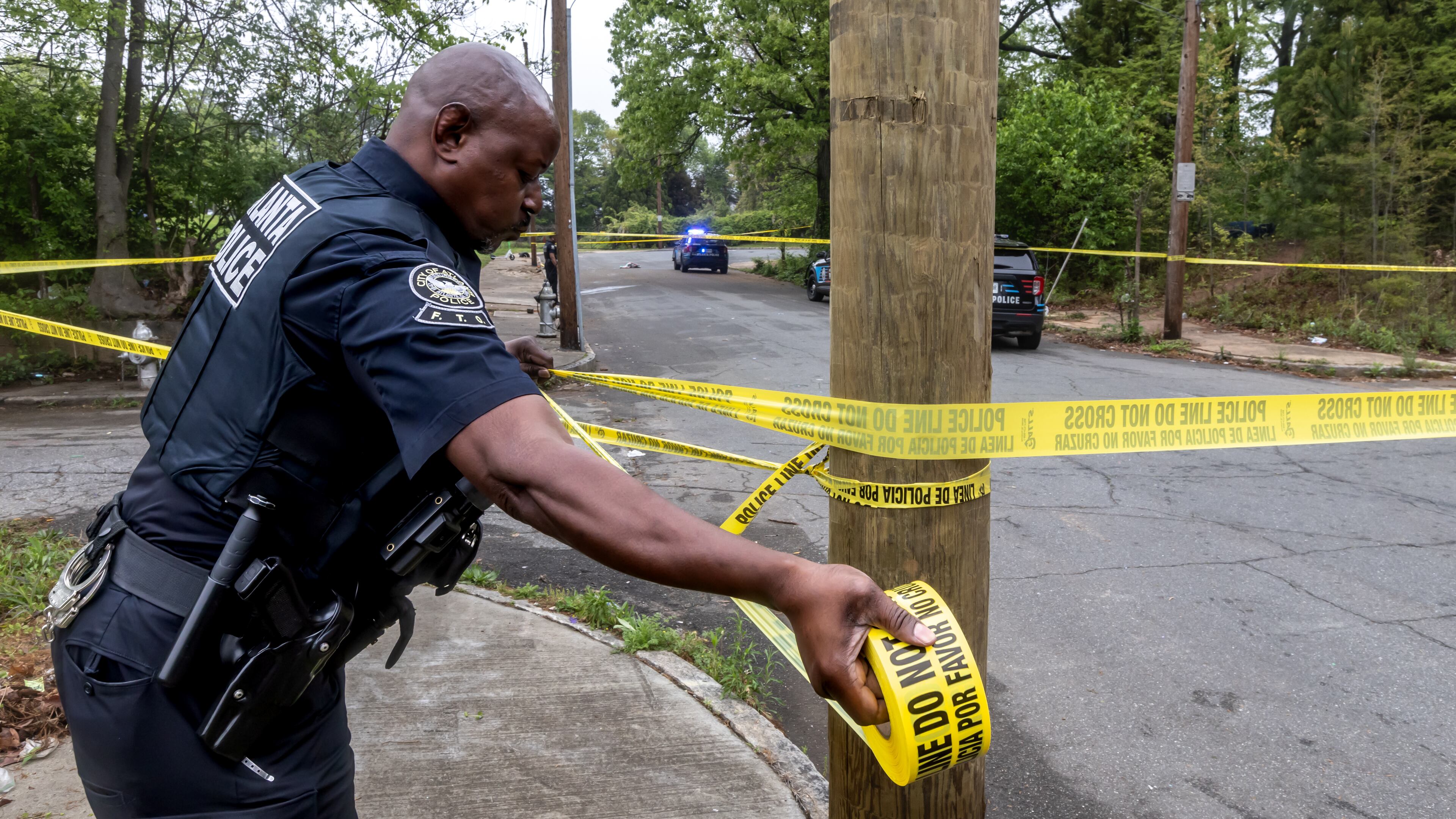 Atlanta police officer R. Mack stretches crime scene tape across Cooper Street on April 10 as police investigate a shooting in southwest Atlanta. (John Spink/The Atlanta Journal-Constitution)