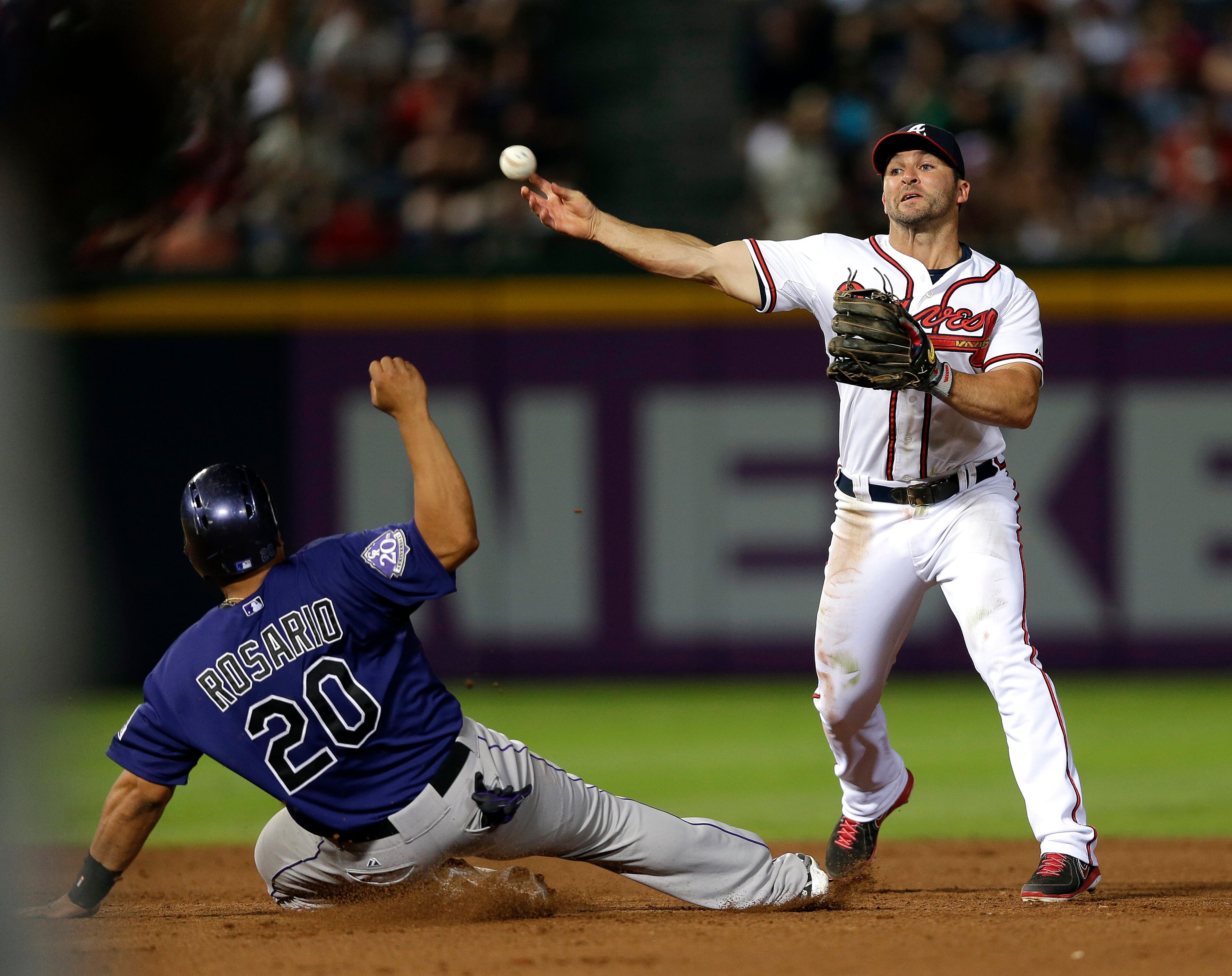 Dan Uggla forces out Colorado Rockies' Wilin Rosario (20) at second base as he turns a double play on a Nolan Arenado ground ball in the eight inning of a baseball game in Atlanta, Monday, July 29, 2013.