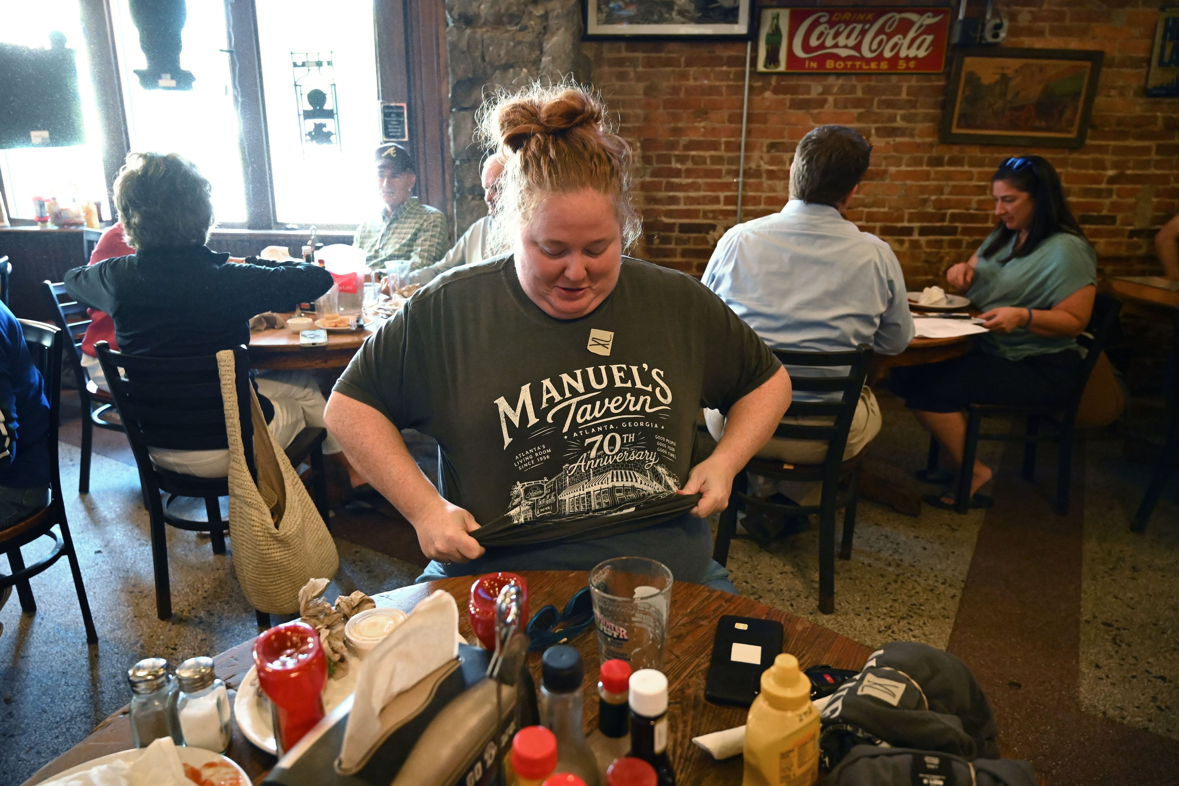 Elizabeth Secrest tries on a 70th anniversary T-shirt during Manuel’s Tavern's 70th anniversary celebration on Thursday, Aug. 6, 2026, in Atlanta. (Hyosub Shin/AJC)