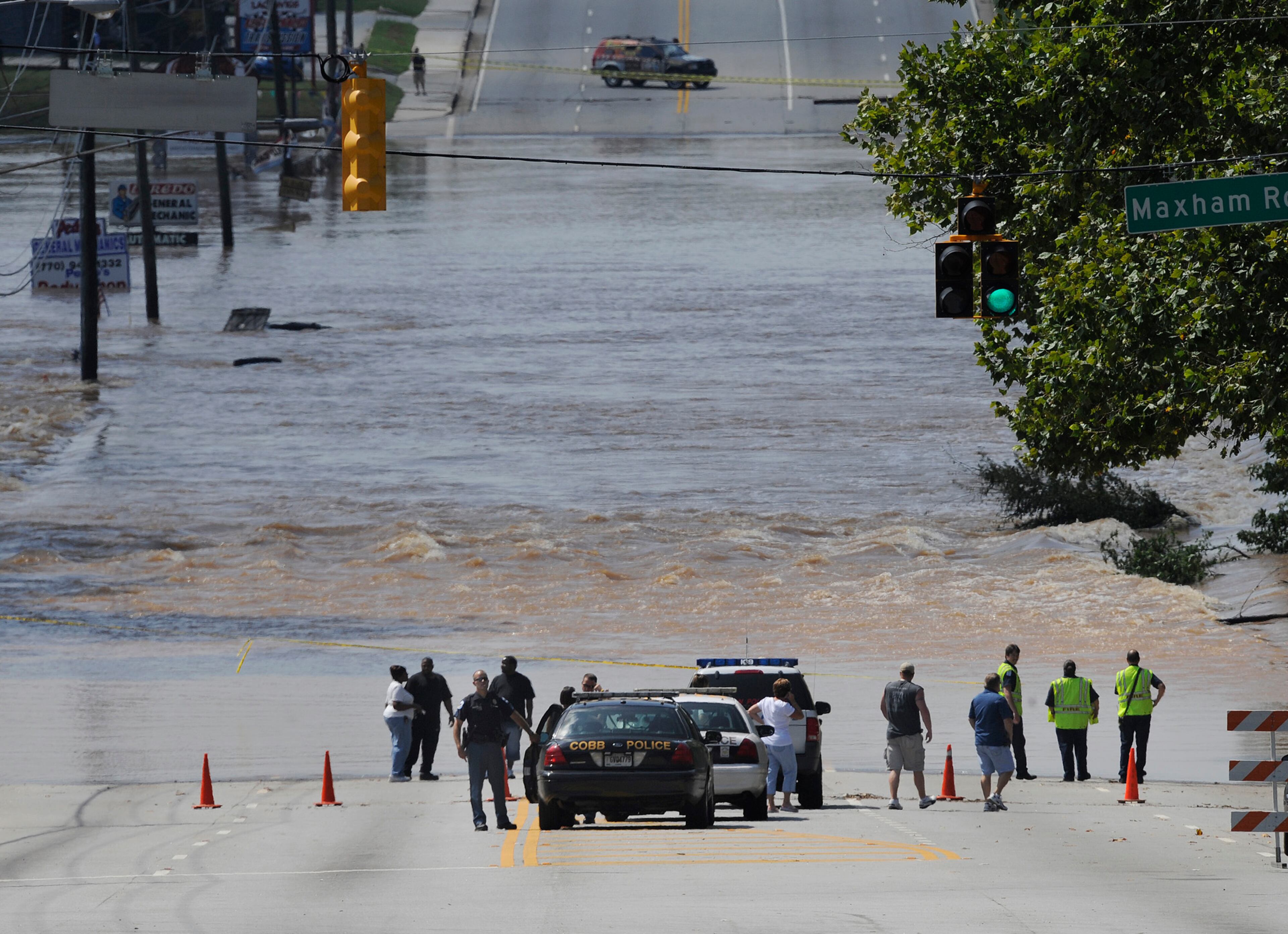 A Cobb County police officer stands guard near his vehicle while onlookers watch as the rapidly moving water from Sweetwater Creek separates Veterans Memorial Highway in Austell on Tuesday, September 22, 2009. The water from the creek has flooded homes, schools and businesses. (Photo: Johnny Crawford/ AJC)