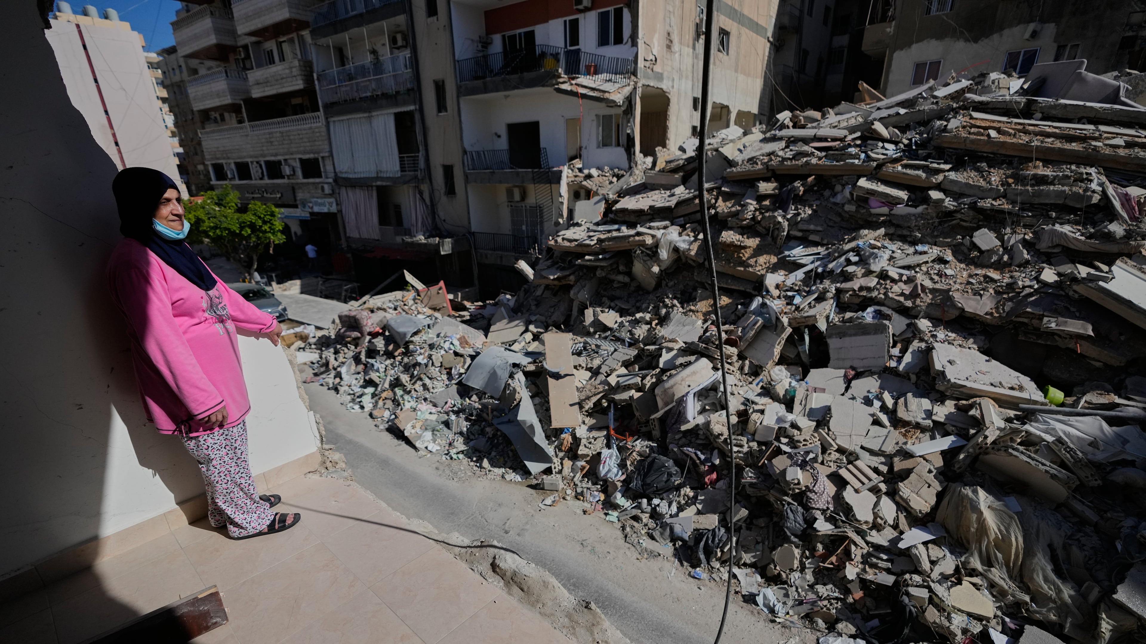 Em Ali Khodor, 75, looks through her damaged apartment into a destroyed building that was hit few weeks ago by an Israeli airstrikeafter she returns to the house, in the southern port city of Tyre, Lebanon, Thursday, April 30, 2026. (AP Photo/Hussein Malla)