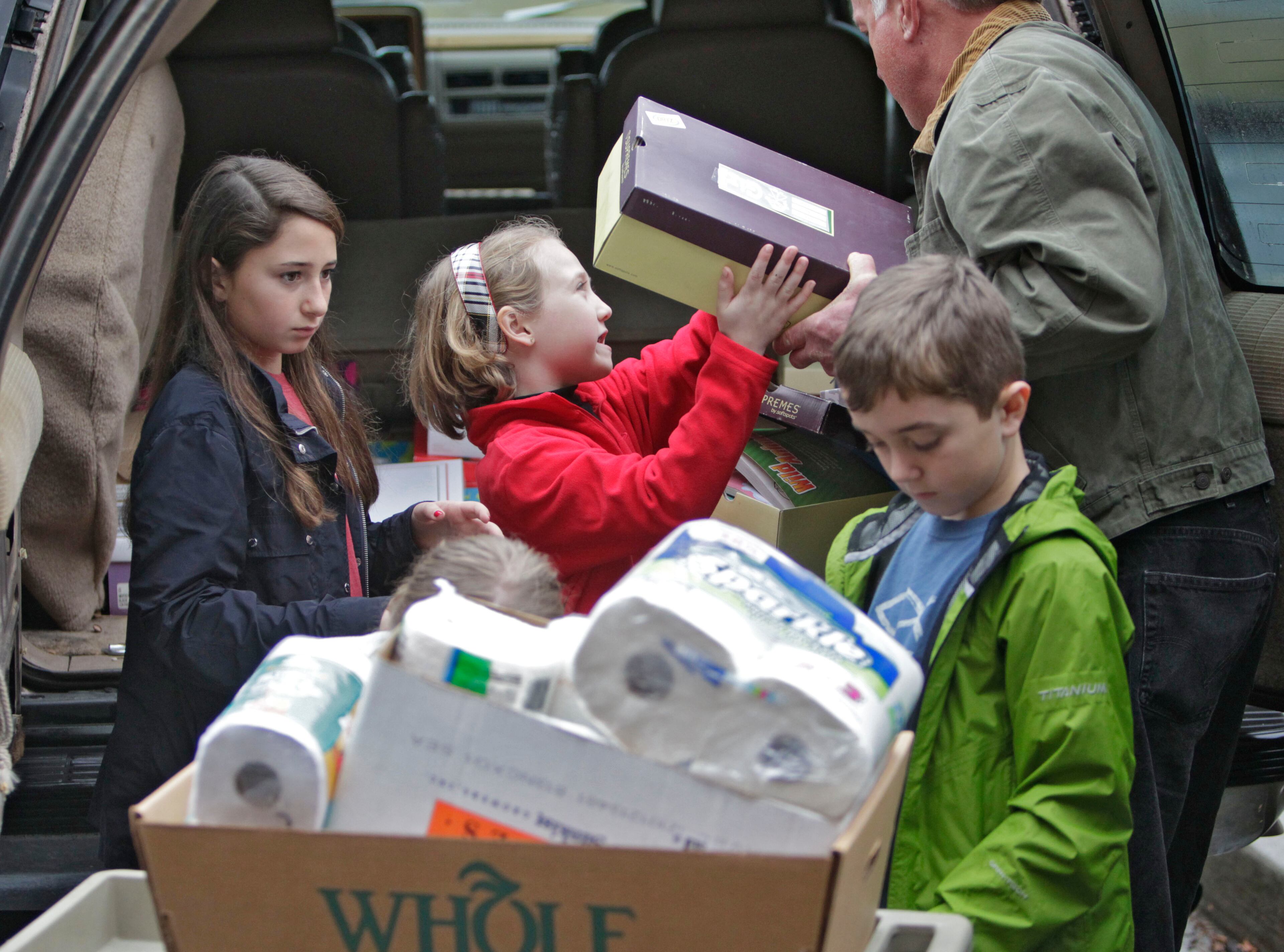 Grace Fragle (from left), 10, Mackenzie Williams, 8, and Jacob Fragle, 10, help Steve Powell load one of the vehicles in the caravan at the Campus Church of Christ in Norcross Dec. 24, 2012.