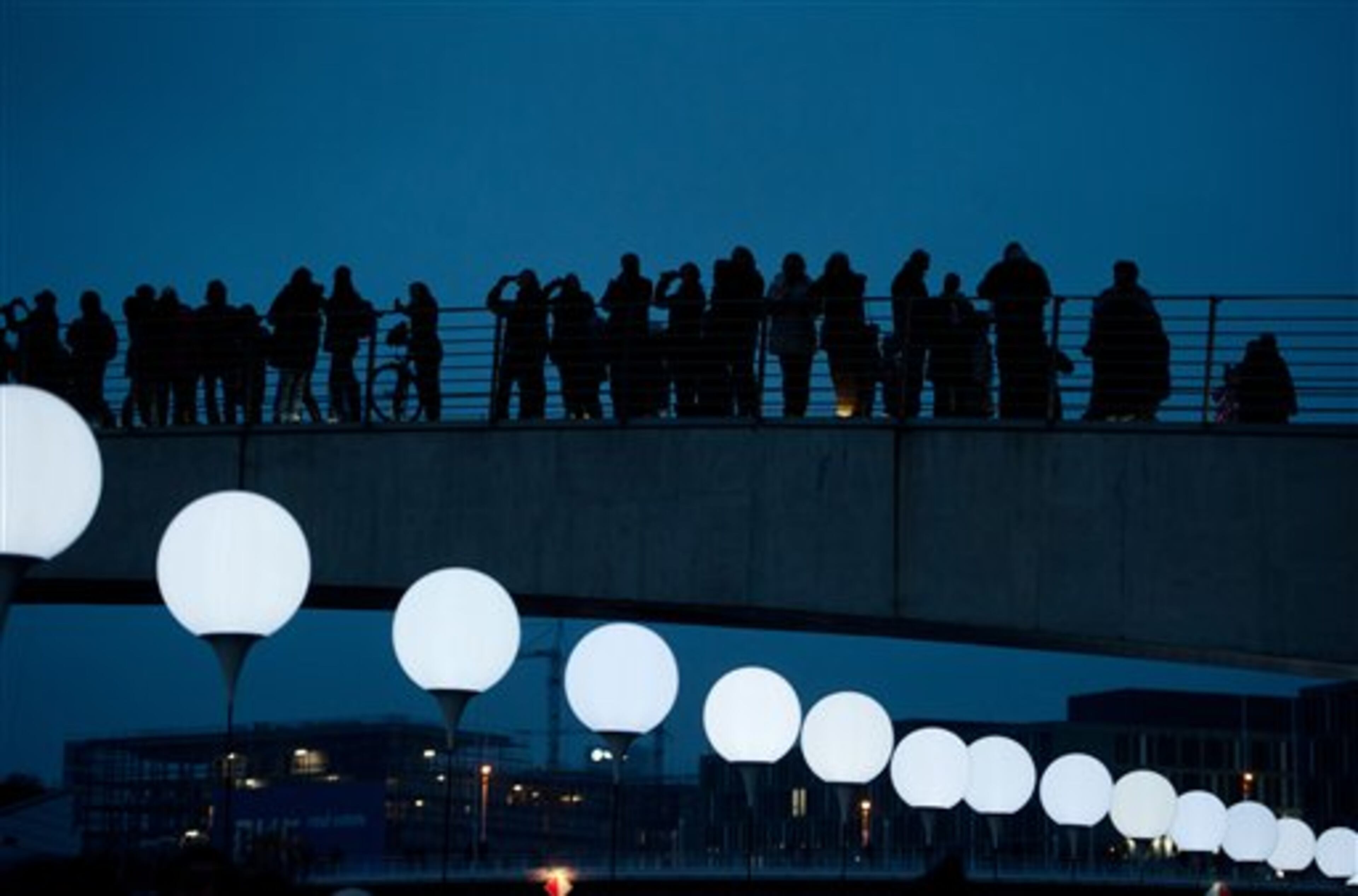 People watch balloons of the art project 'Lichtgrenze 2014' ('lightborder 2014') in Berlin, Germany, Sunday, Nov. 9, 2014. The light installation featuring 8,000 luminous white balloons commemorates the division of Berlin where the 25th anniversary of the fall of the wall is marked with numerous events. On Nov. 9, 1989 - the East-German government lifted travel restrictions and thousands of East Berliners had pushed their way past perplexed border guards to celebrate freedom with their brethren in the West. (AP Photo/Steffi Loos)