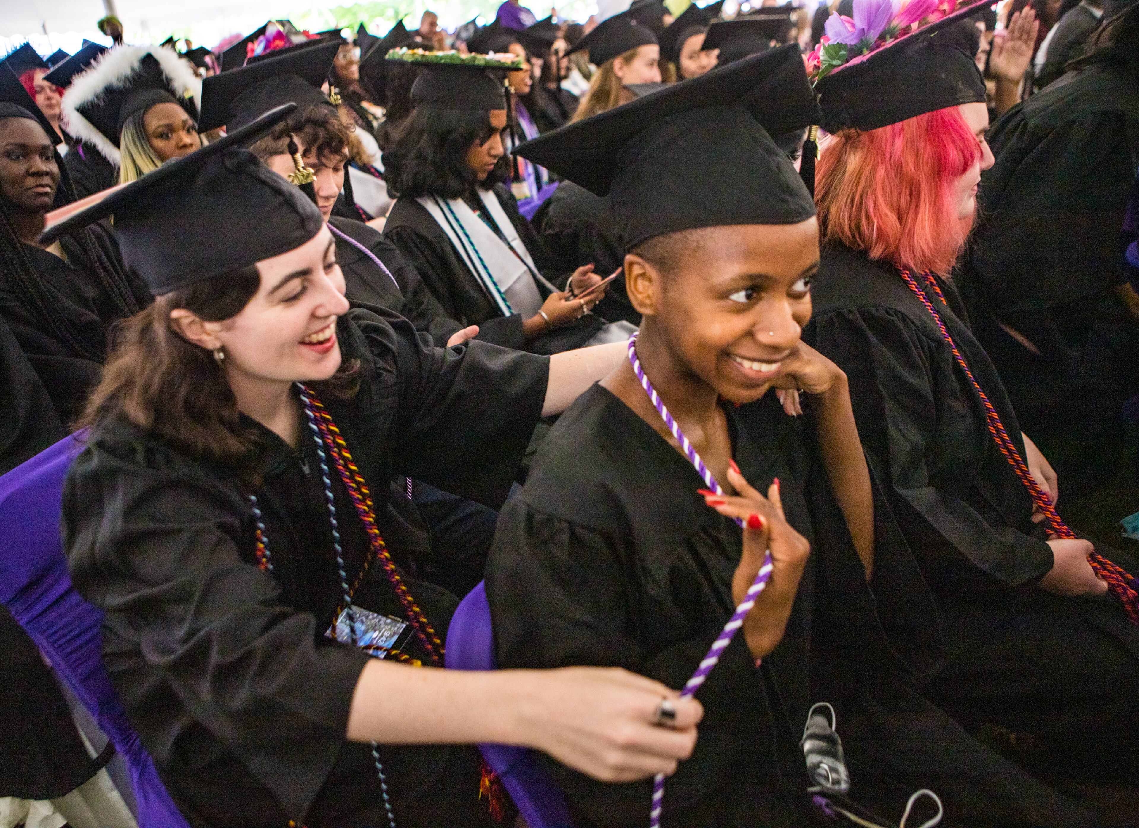 Elizabeth Edwards, left, give one of her cords to classmate Lyrick Courtney during Agnes Scott College graduation ceremony on Saturday, May 14, 2022. (Jenni Girtman for The Atlanta Journal-Constitution)