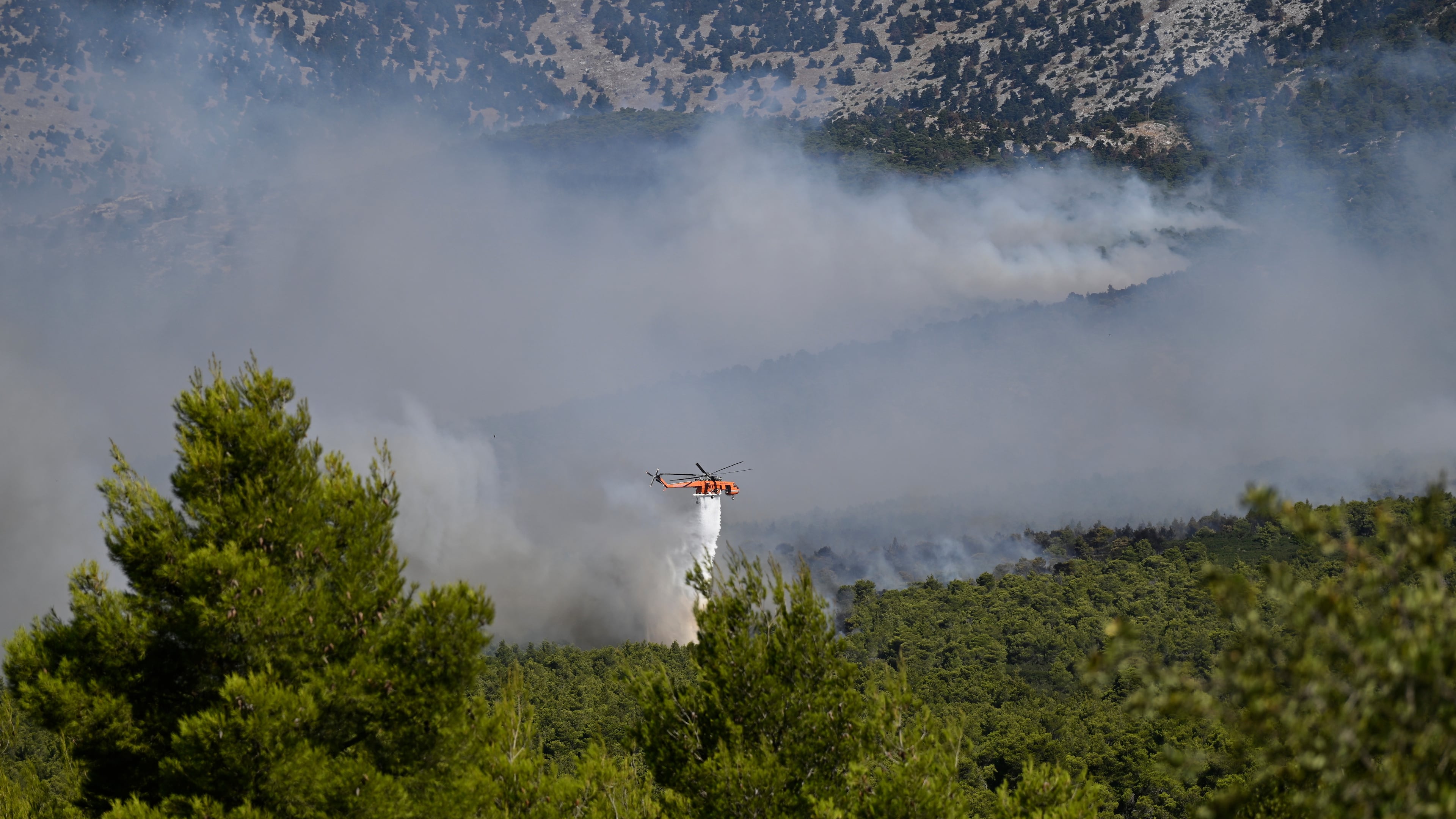 A firefighting helicopter drops water over a smoke-filled forest during a wildfire near Porto Germeno, northwest of Athens, Greece, Sunday, Aug. 2, 2026. (AP Photo/Michael Varaklas)