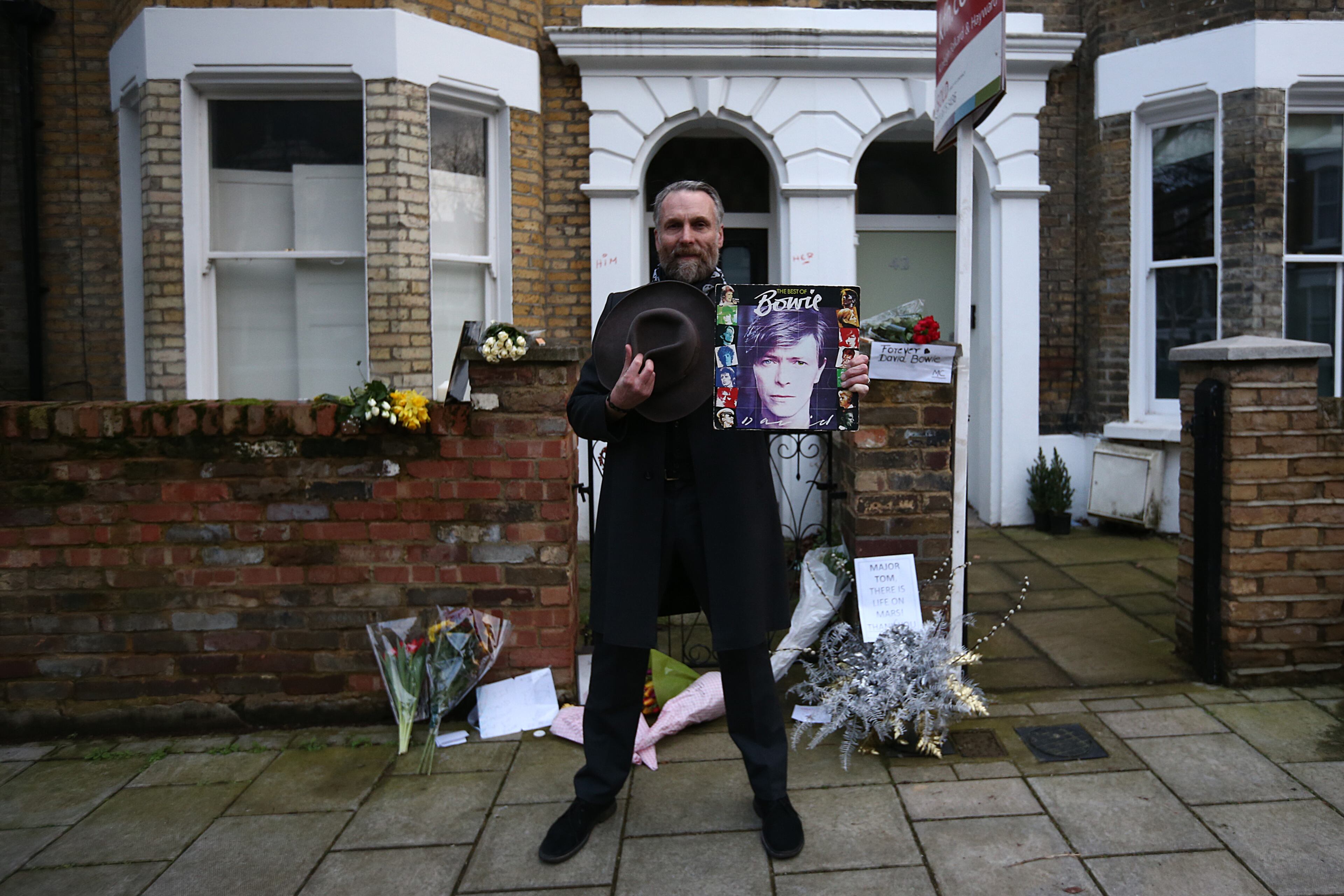 LONDON, ENGLAND - JANUARY 11: A fan poses for a photograph with a record outside the boyhood home of David Bowie in Brixton on January 11, 2016 in London, England. British music and fashion icon David Bowie died earlier today at the age of 69 after a battle with cancer. (Photo by Carl Court/Getty Images)