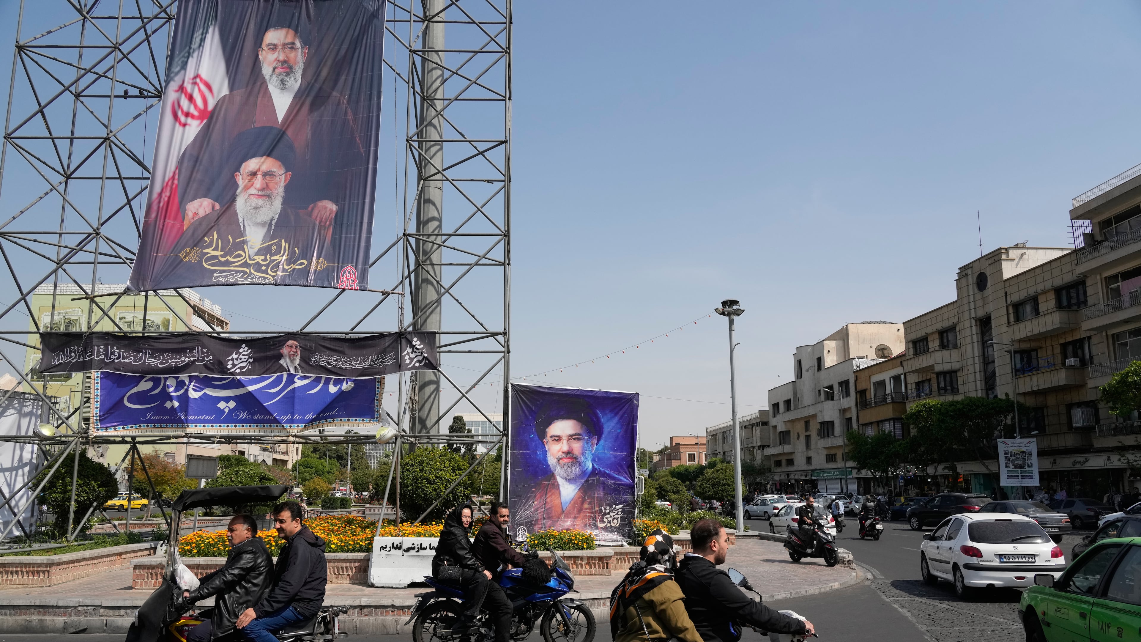 People drive their motorbikes past billboards showing the Iran's Supreme Leader Ayatollah Mojtaba Khamenei, top and right, and his father, the slain Supreme Leader Ayatollah Ali Khamenei, who was killed in U.S. and Israeli strikes on Feb. 28, in downtown Tehran, Iran, Thursday, April 16, 2026. (AP Photo/Vahid Salemi)