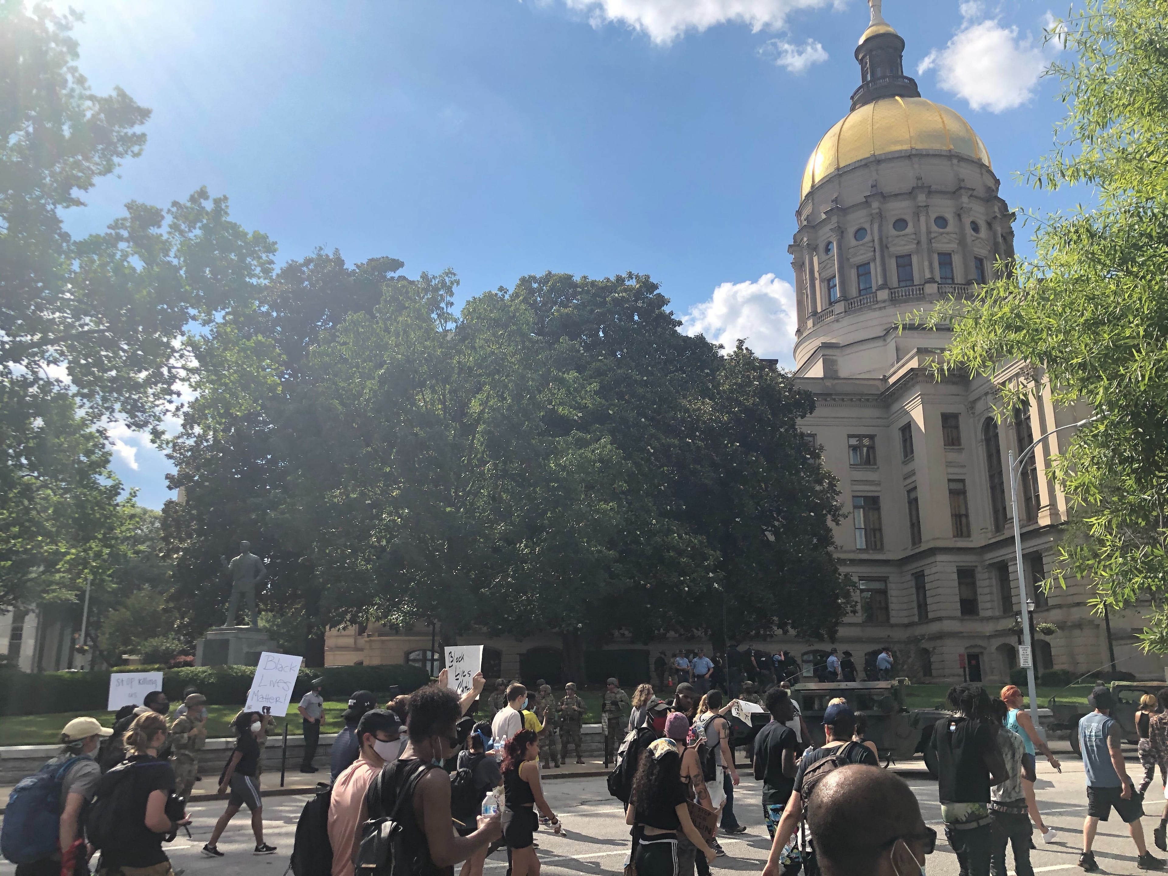 A large group of protestors march past the Georgia State Capitol, which is ringed by dozens of National Guard members and law officers.