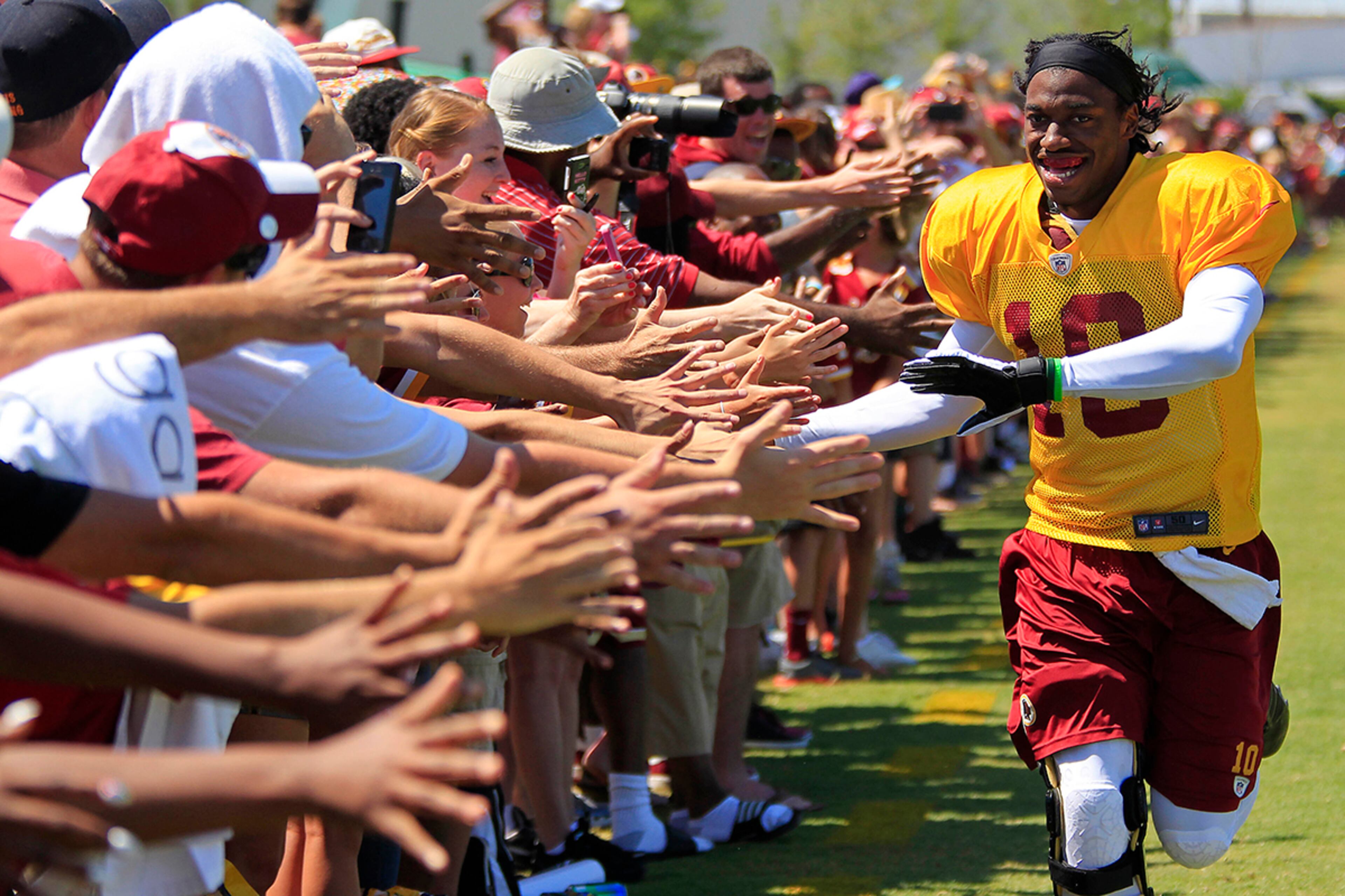 Washington Redskins quarterback Robert Griffin III (10) runs down the sidelines to shake hands with fans prior to afternoon practice during training camp at the Bon Secours Washington Redskins Training Center.